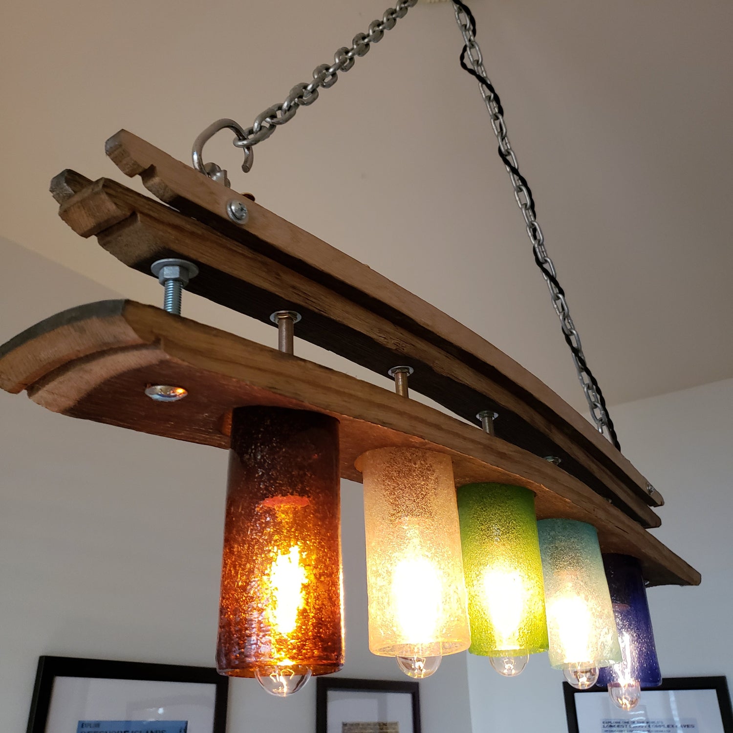 Image of a light fixture repurposed from barrel staves and art glass, lit up and hanging from a ceiling.