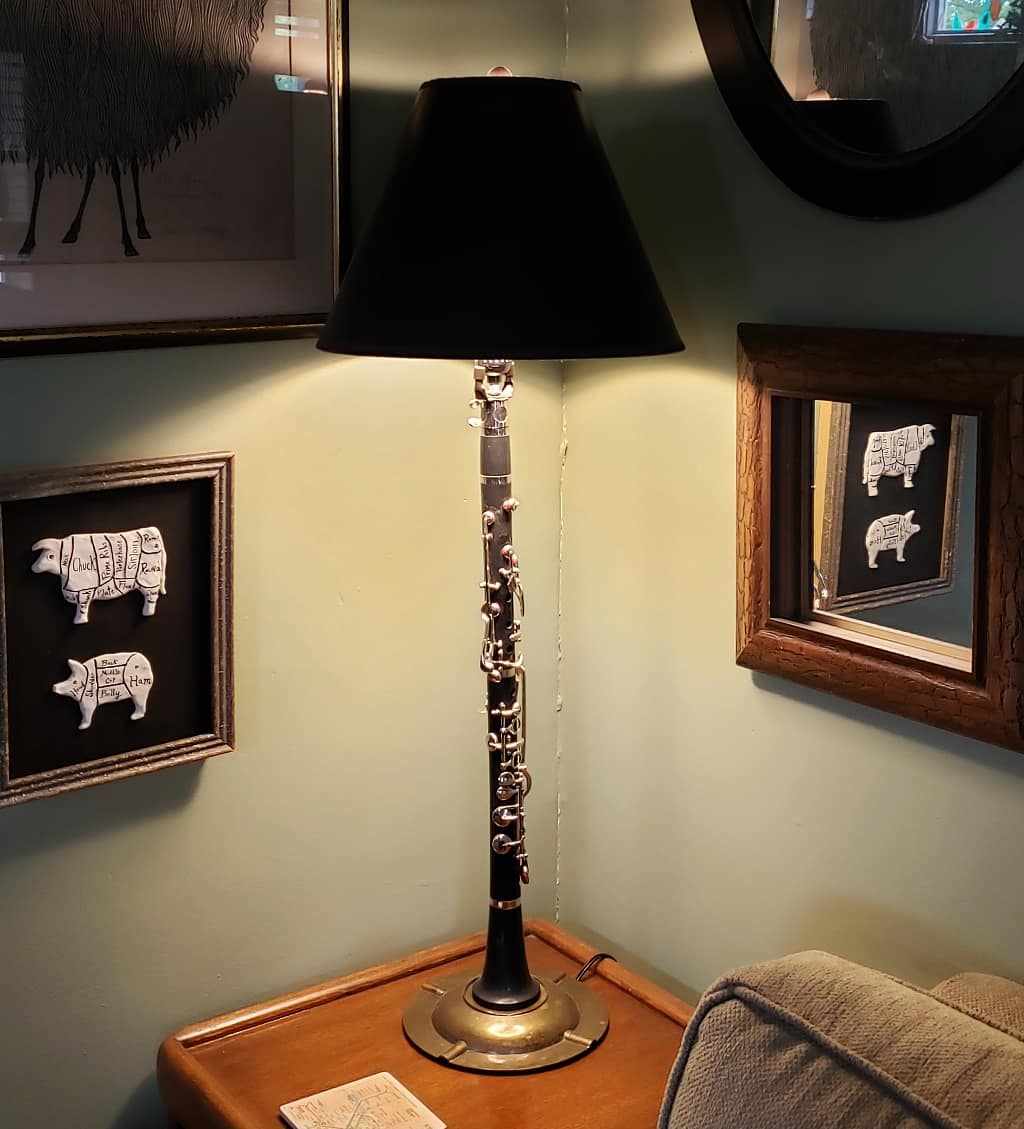 Black clarinet with silver keys repurposed into a table lamp with black shade, mounted on a brass ashtray base.