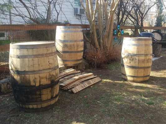 Three wooden barrels on a grassy area with trees and a building in the background.