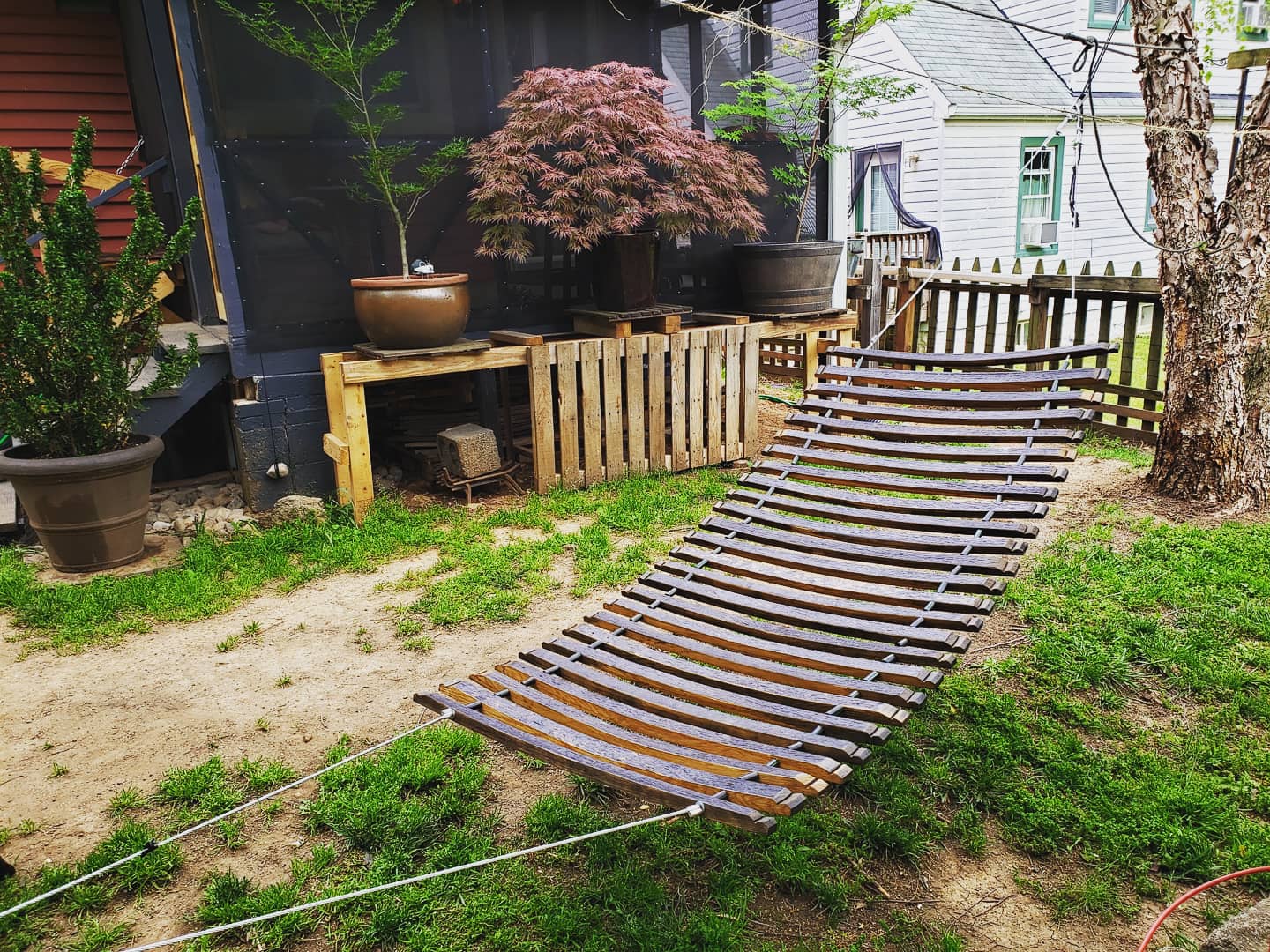 Wooden hammock in a backyard setting with plants and a fence.
