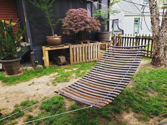 Wooden hammock in a backyard setting with plants and a fence.