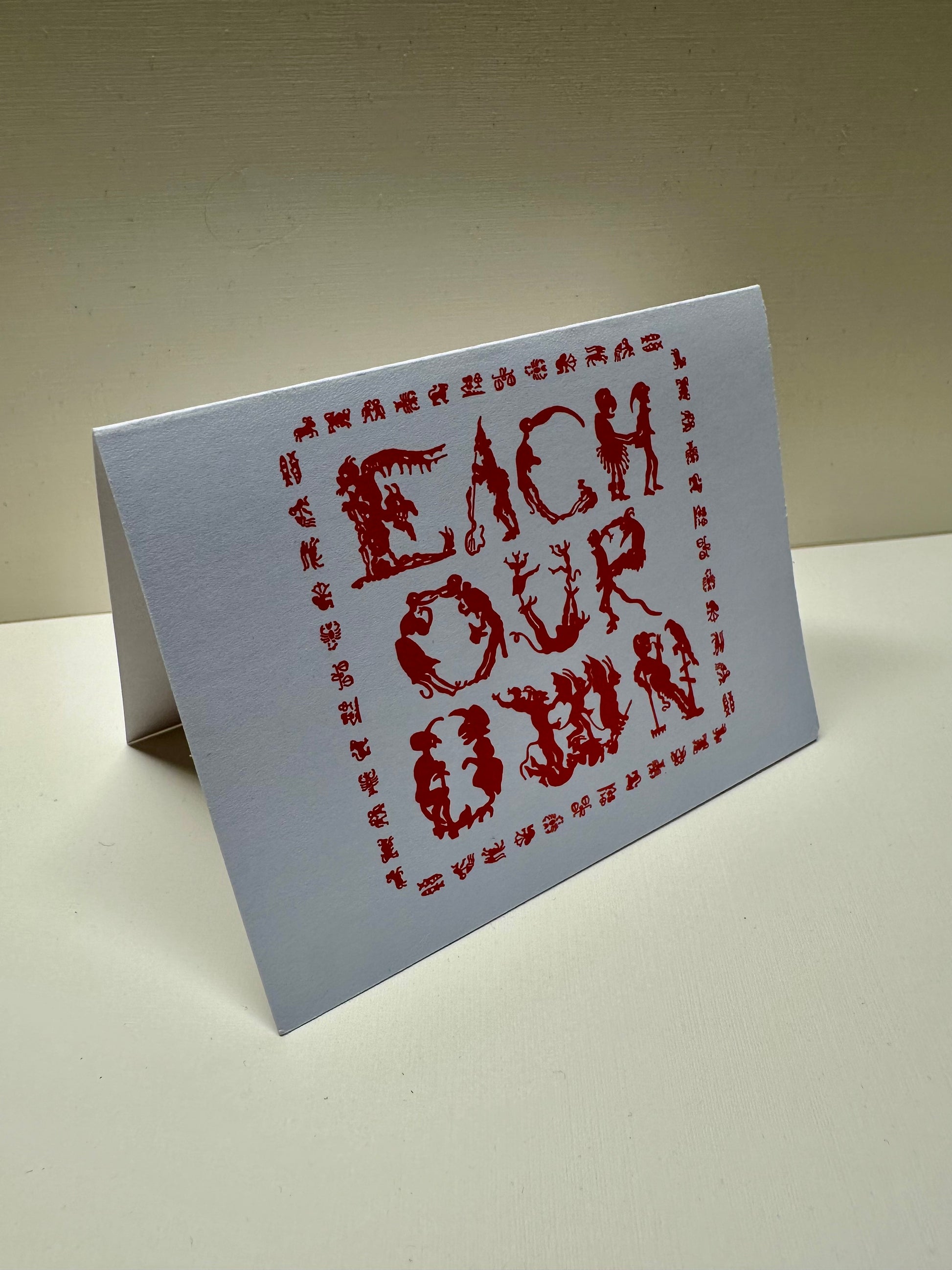 Front view of the 'Each Our Own' greeting card. Folded in half in landscape orientation.