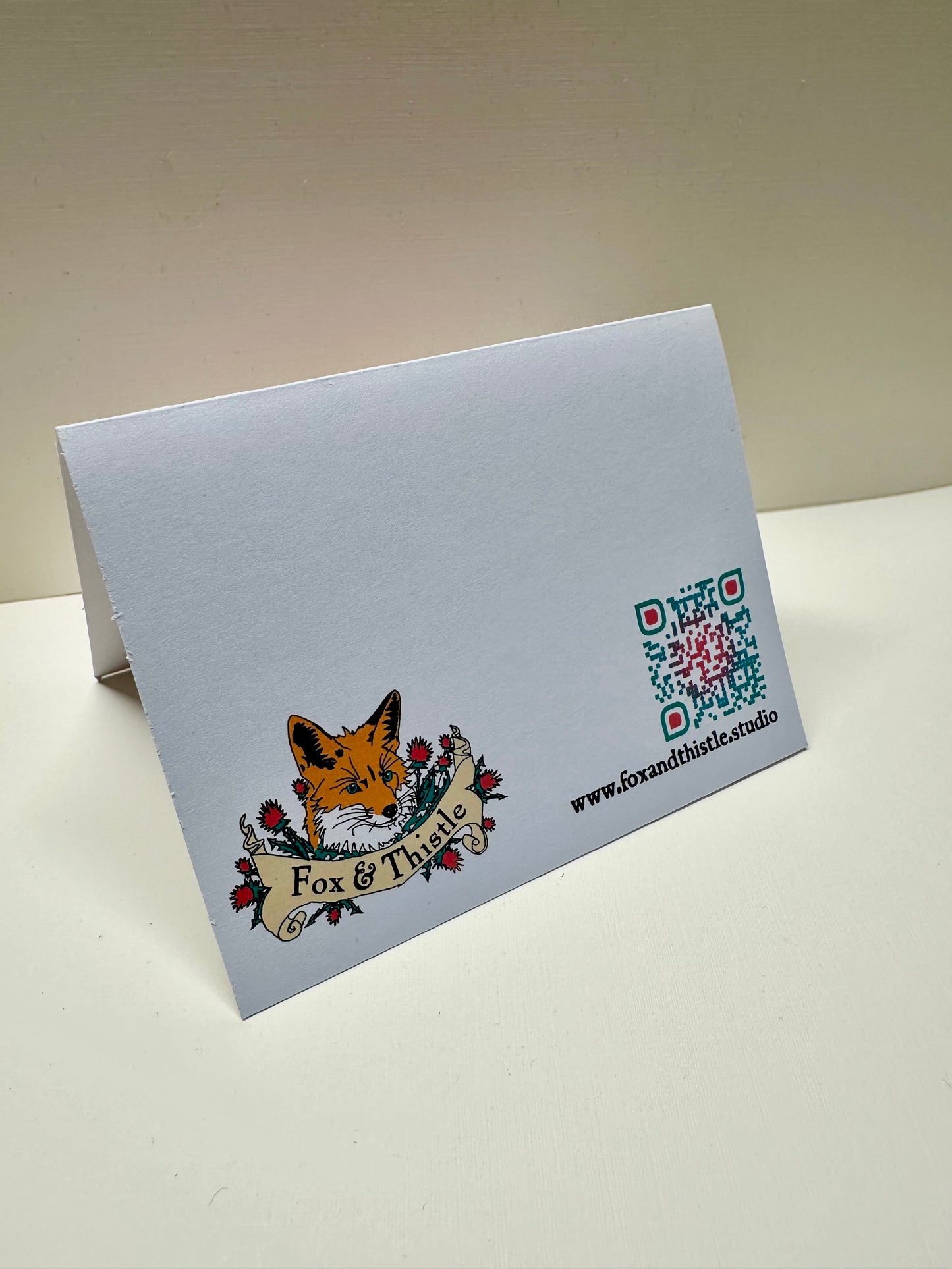 Back of 'Each Our Own' card featuring the studio logo, website, and QR code.