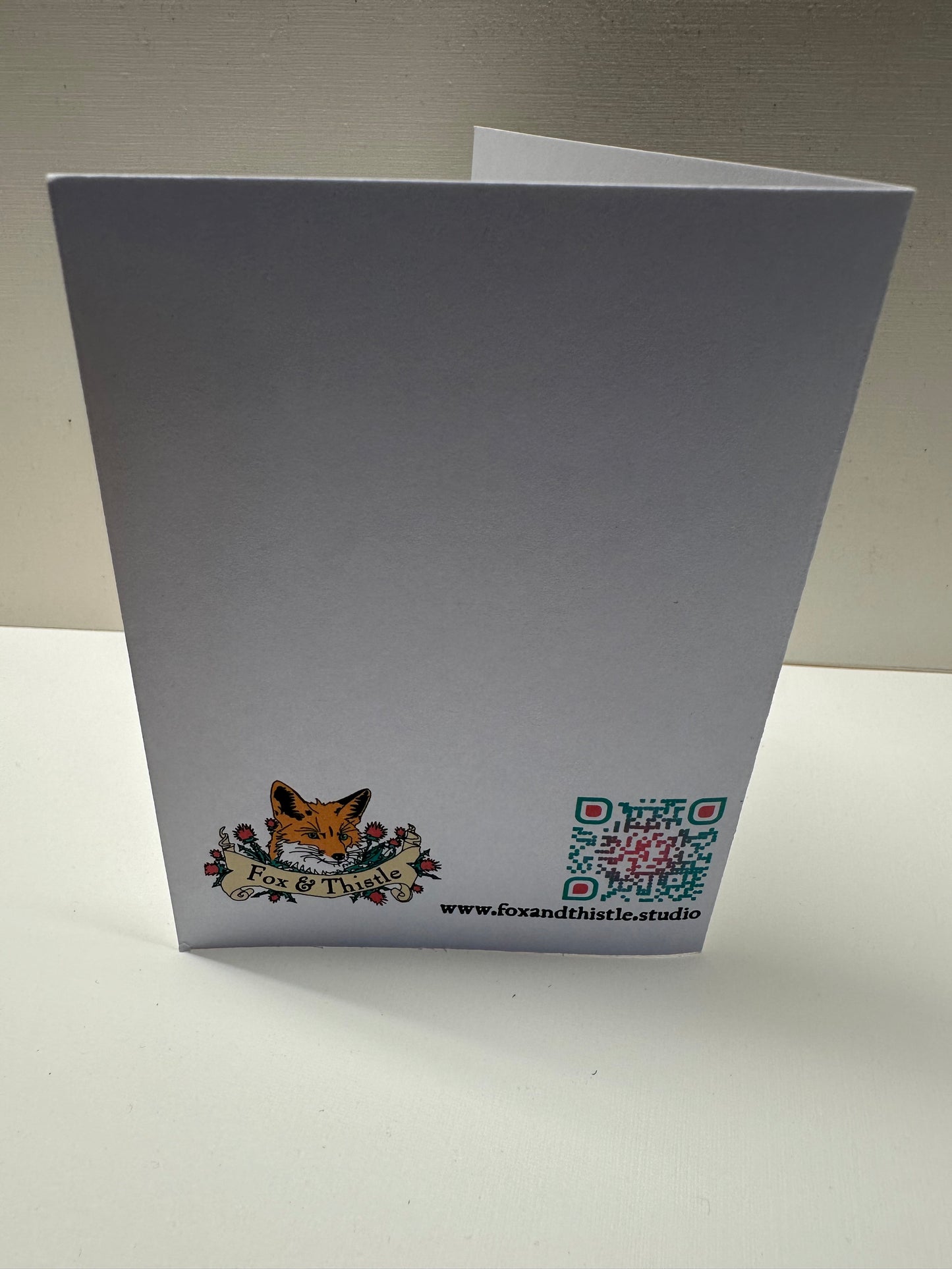 Back view of 'fool at a banquet' greeting card. Features studio web address, QR code, and logo.