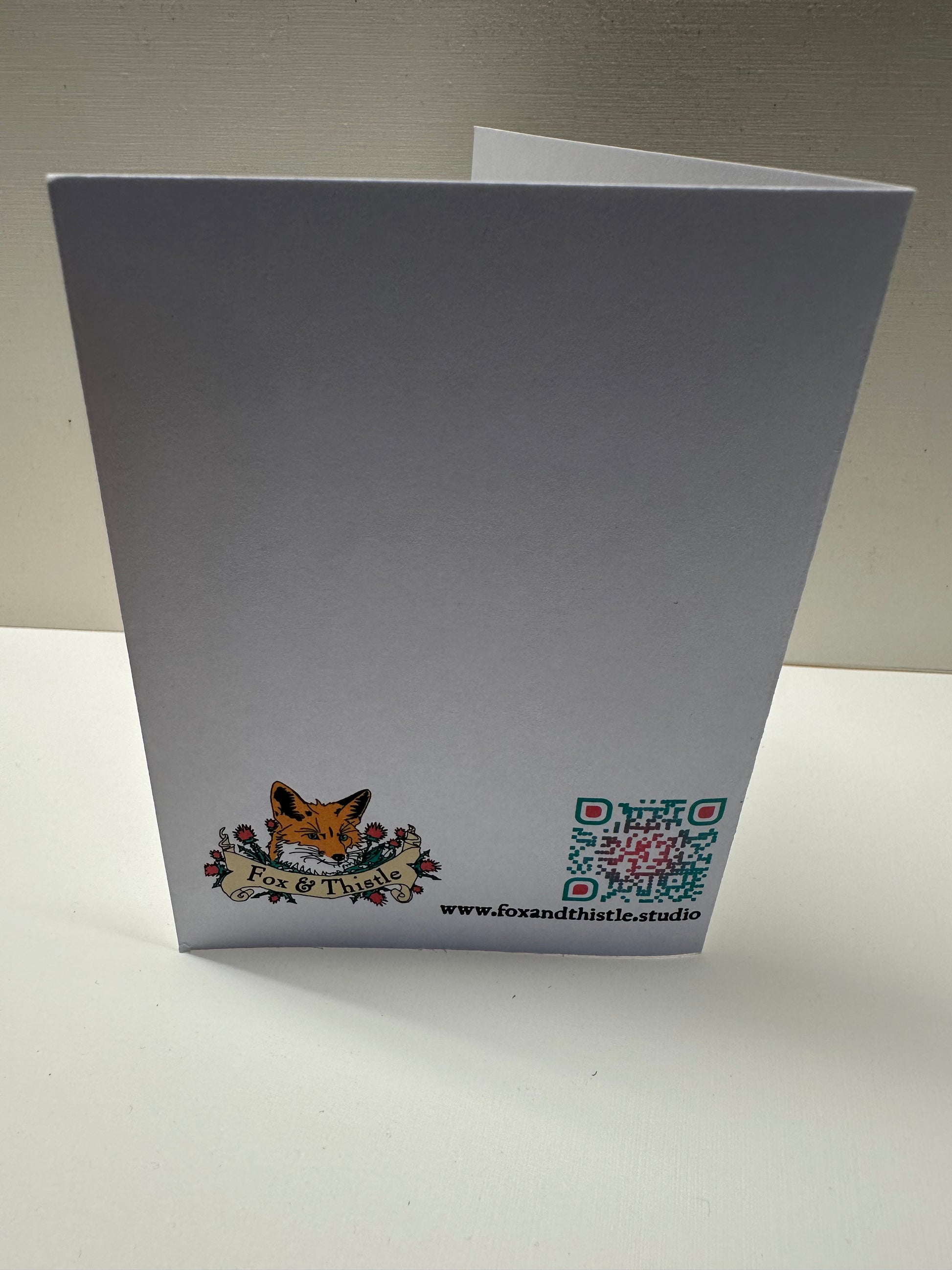 Back view of 'fool at a banquet' greeting card. Features studio web address, QR code, and logo.