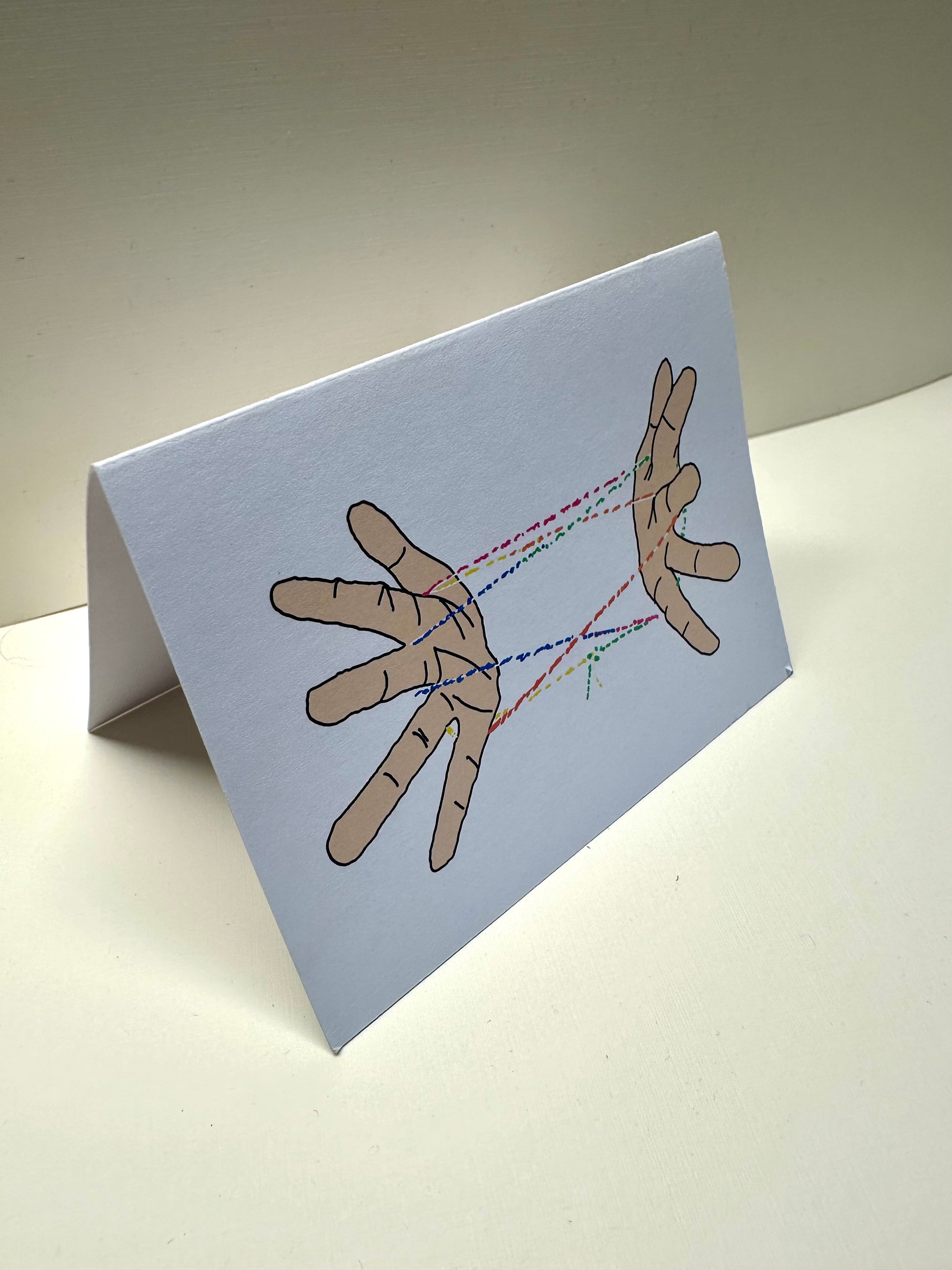 Front perspective of 'Cat's Cradle Card' illustration. It is folded in half long way.