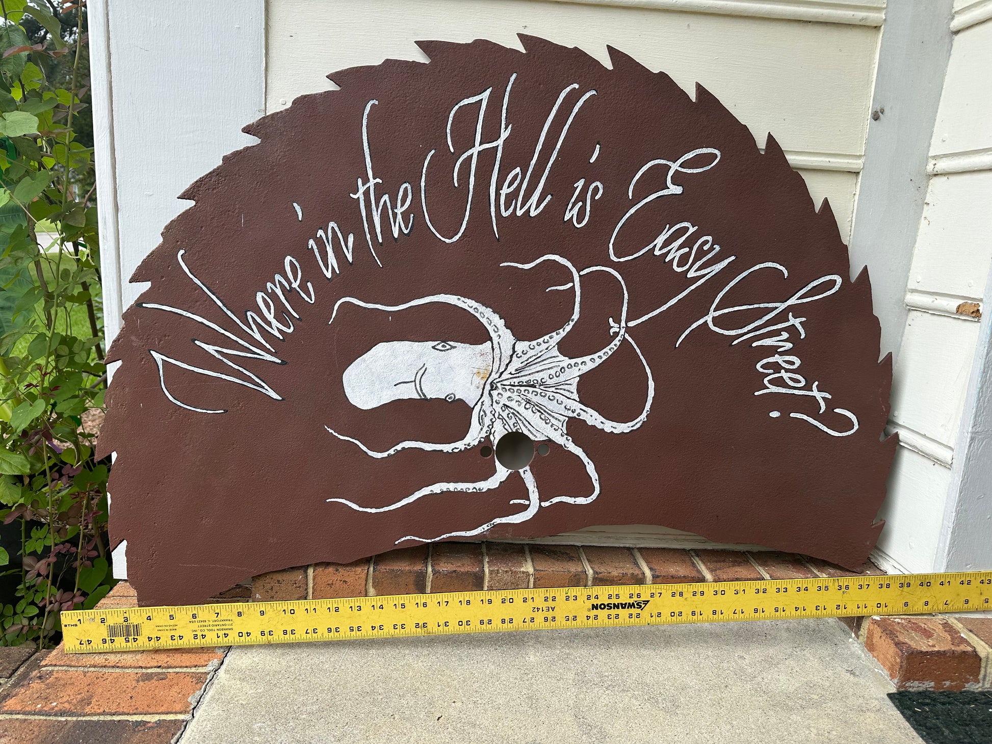 Decorative sign with text and octopus design, measured with a tape measure.