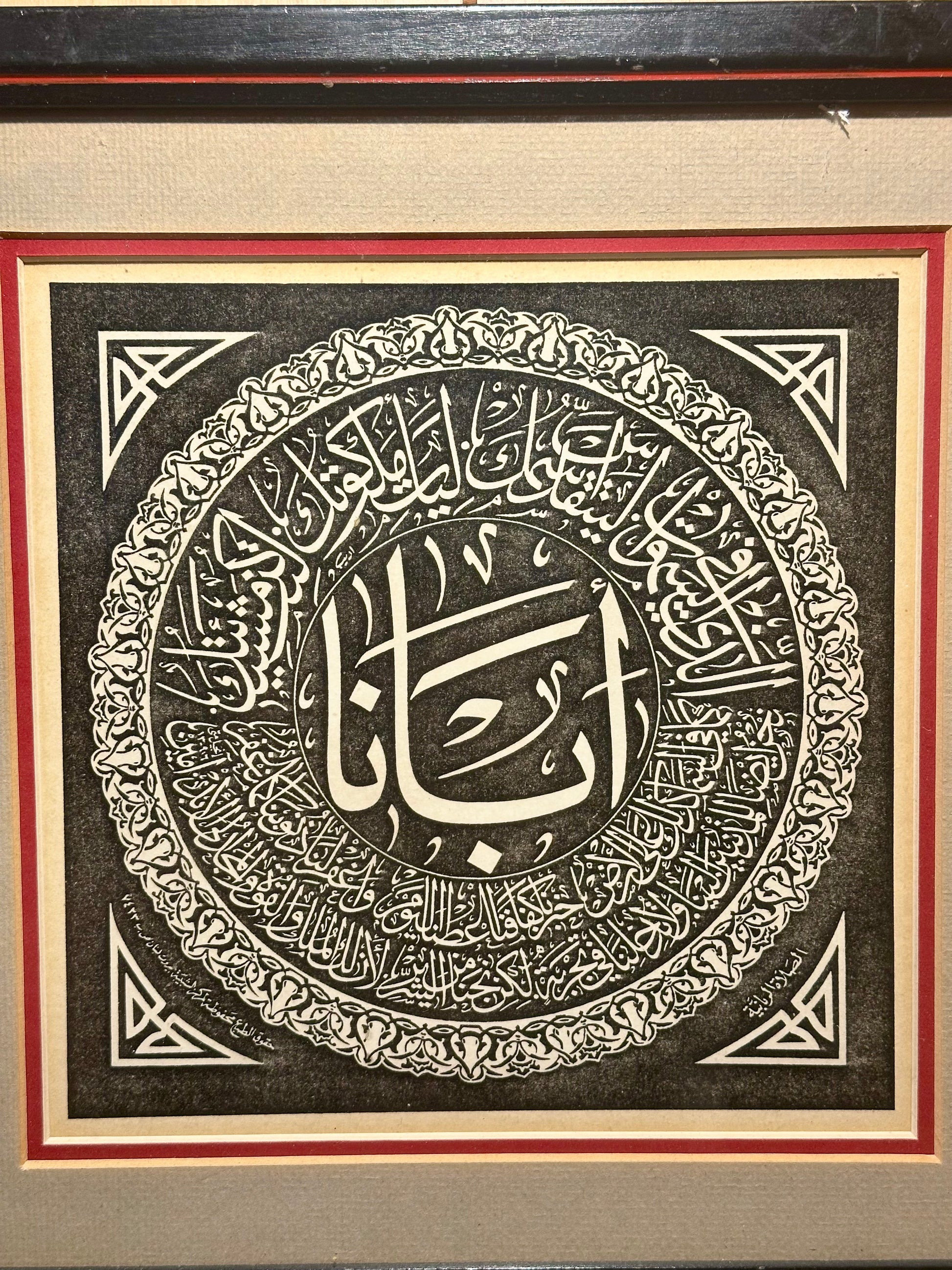 Decorative piece with Arabic calligraphy in a circular design, framed with a red border.