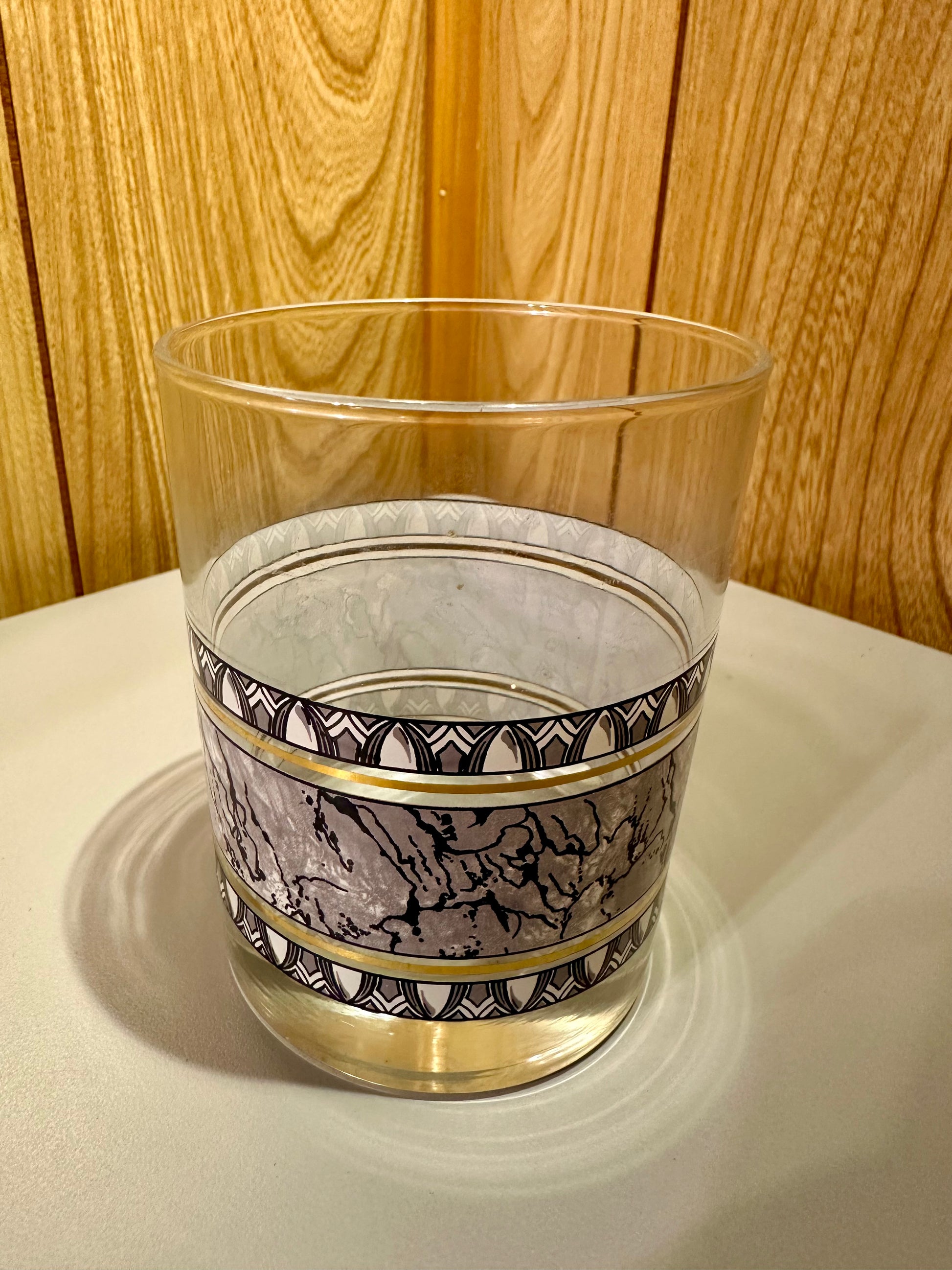 A single glass with decorative band on a gray surface and wooden background