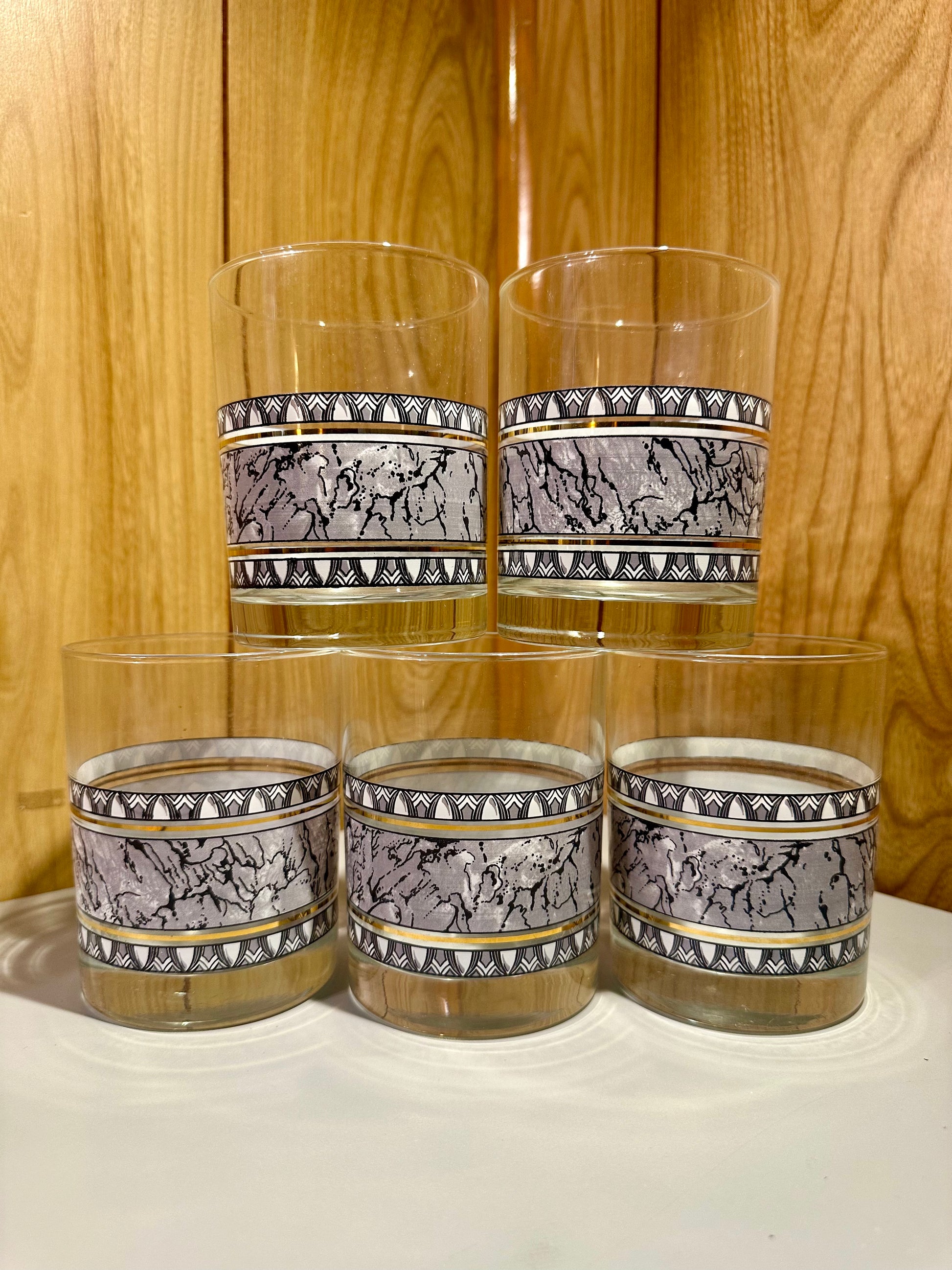 Set of five glass tumblers with decorative bands against a wooden surface