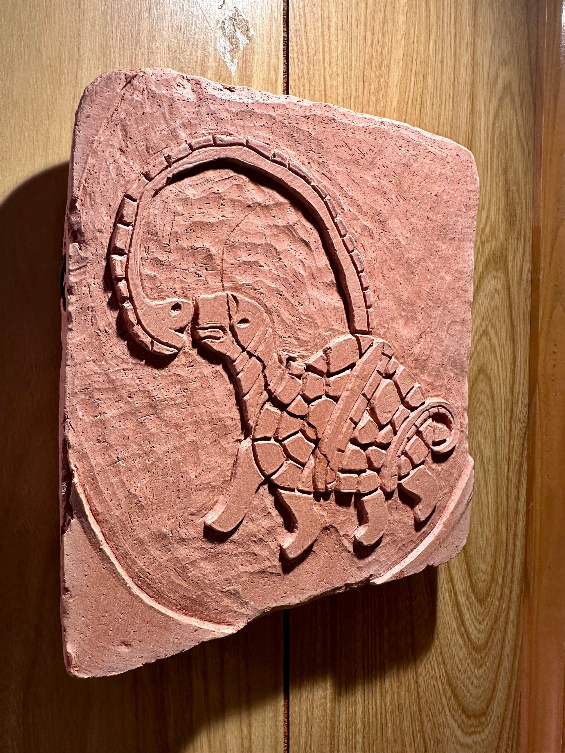 Decorative clay tile with a turtle and snake design on a wooden surface