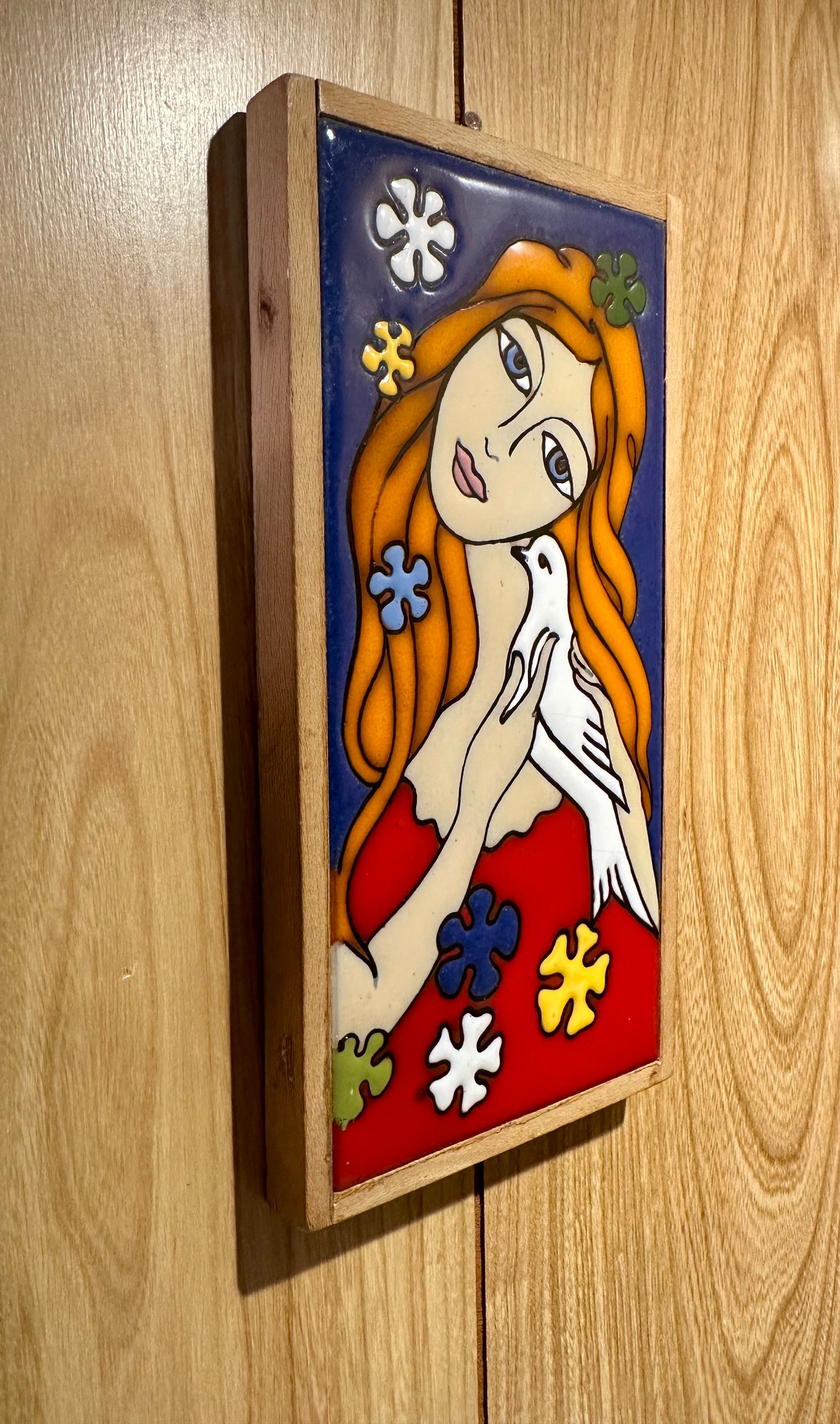 Angled view of decorative wall art with a maiden holding a dove on a wooden panel.