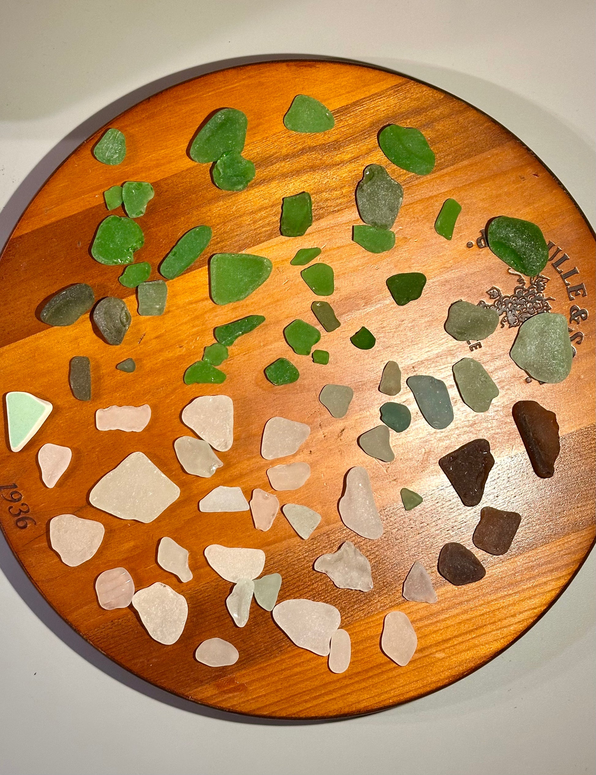 Collection of green and multicolored sea glass on a wooden board.
