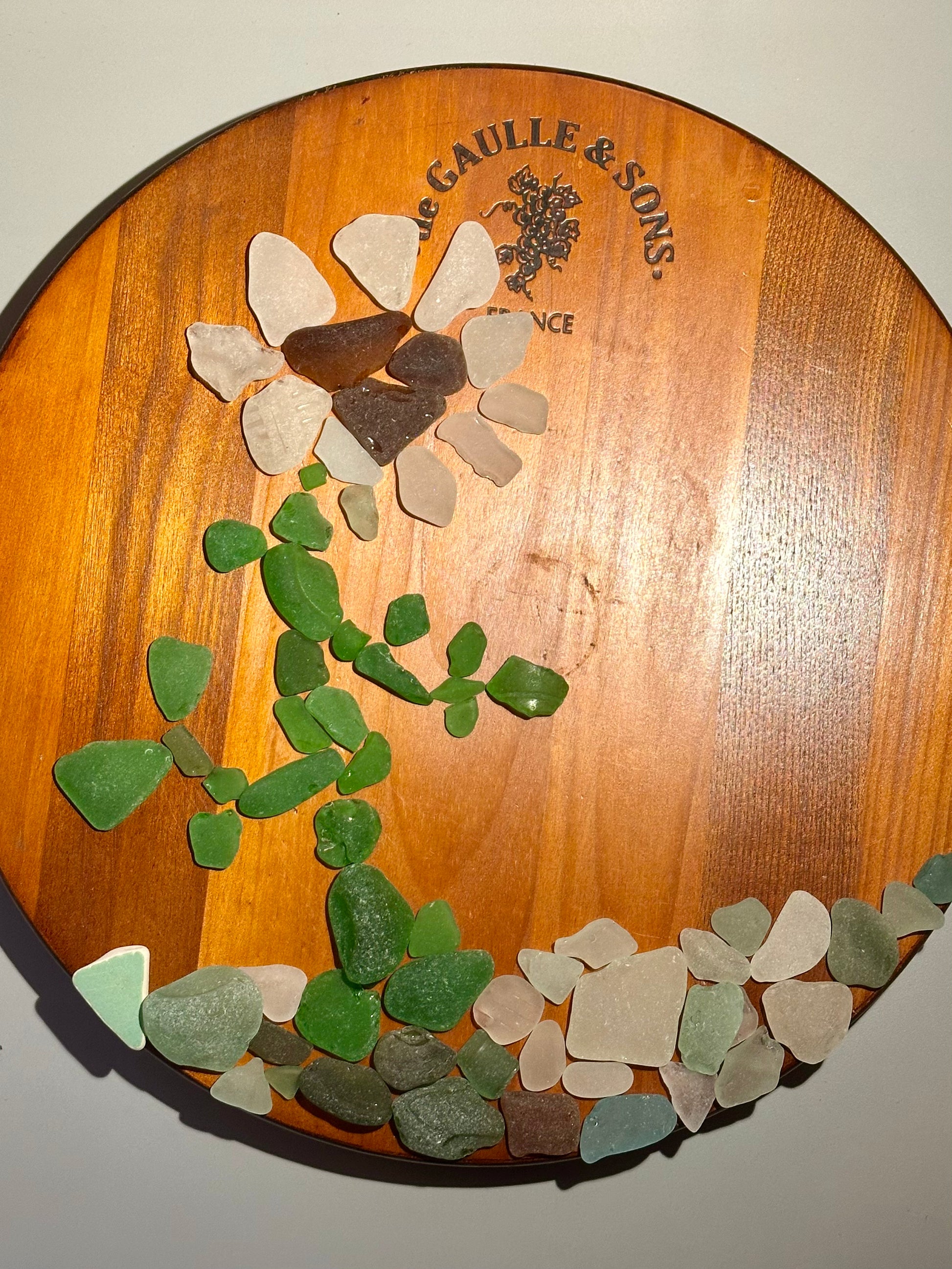 Decorative plate with a flower made of sea glass on a wooden background with 'Gaulle & Sons' branding.