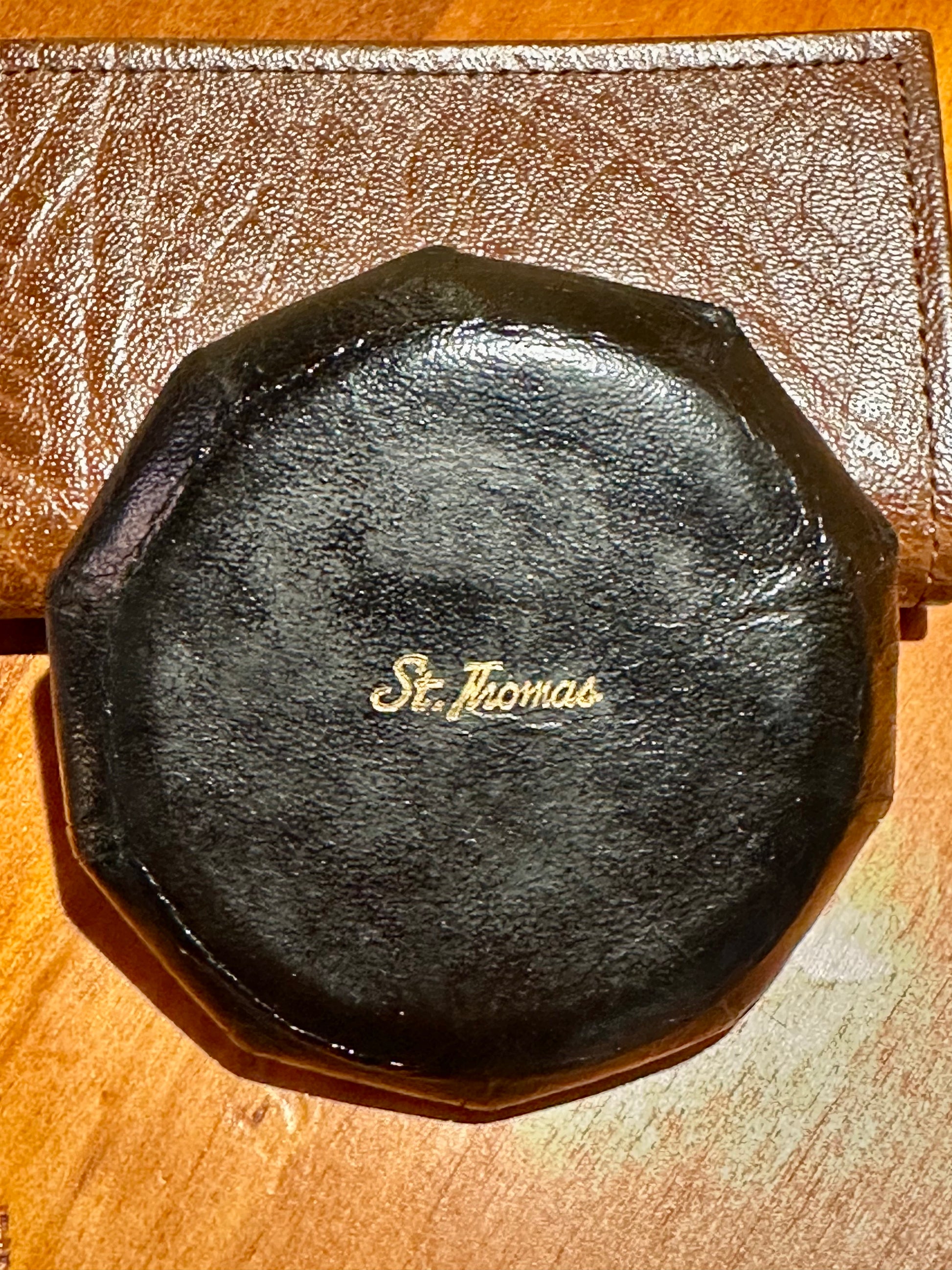 Black leather product with 'St. Thomas' branding on a wooden surface