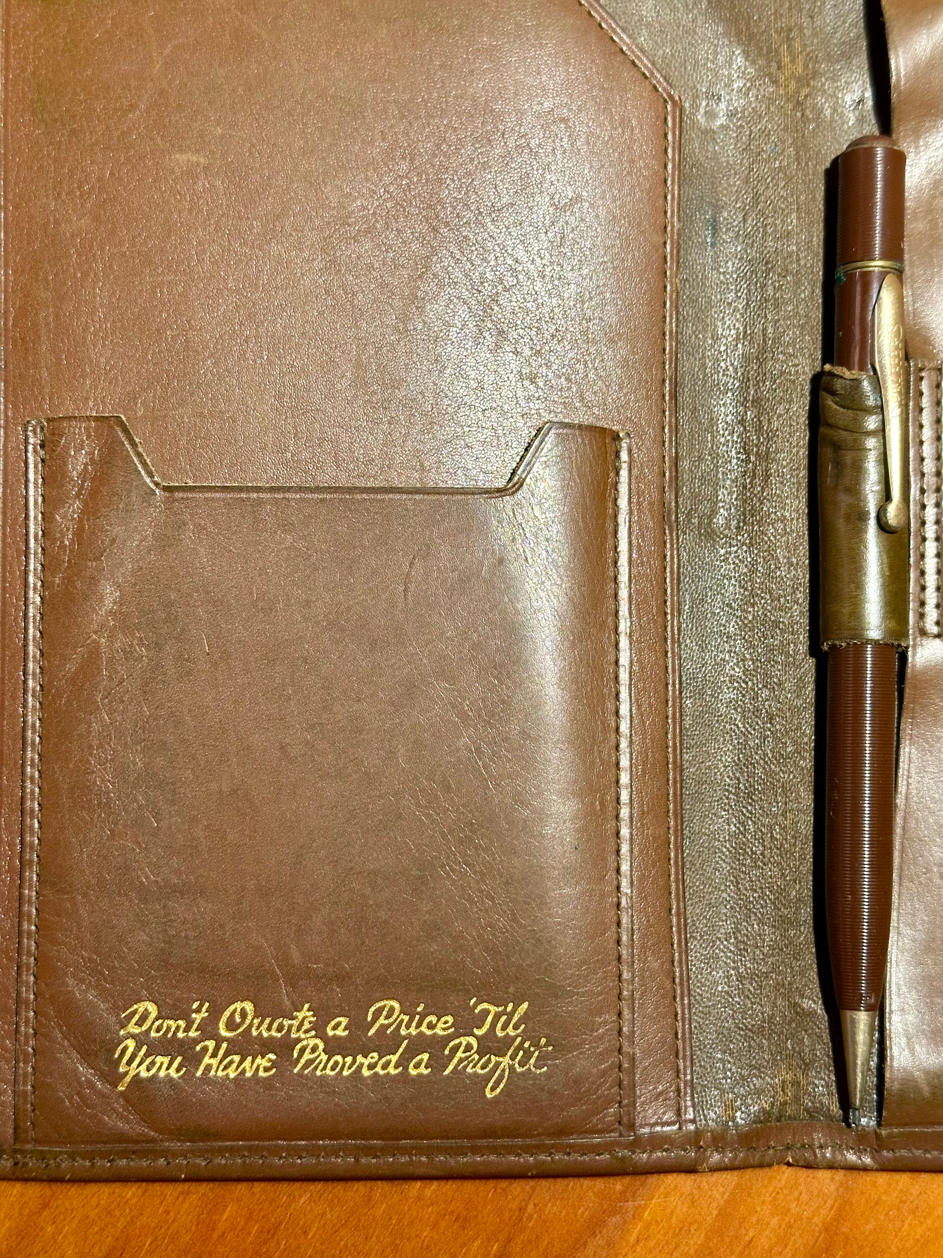 Brown leather notebook with pen holder and quote on a wooden surface