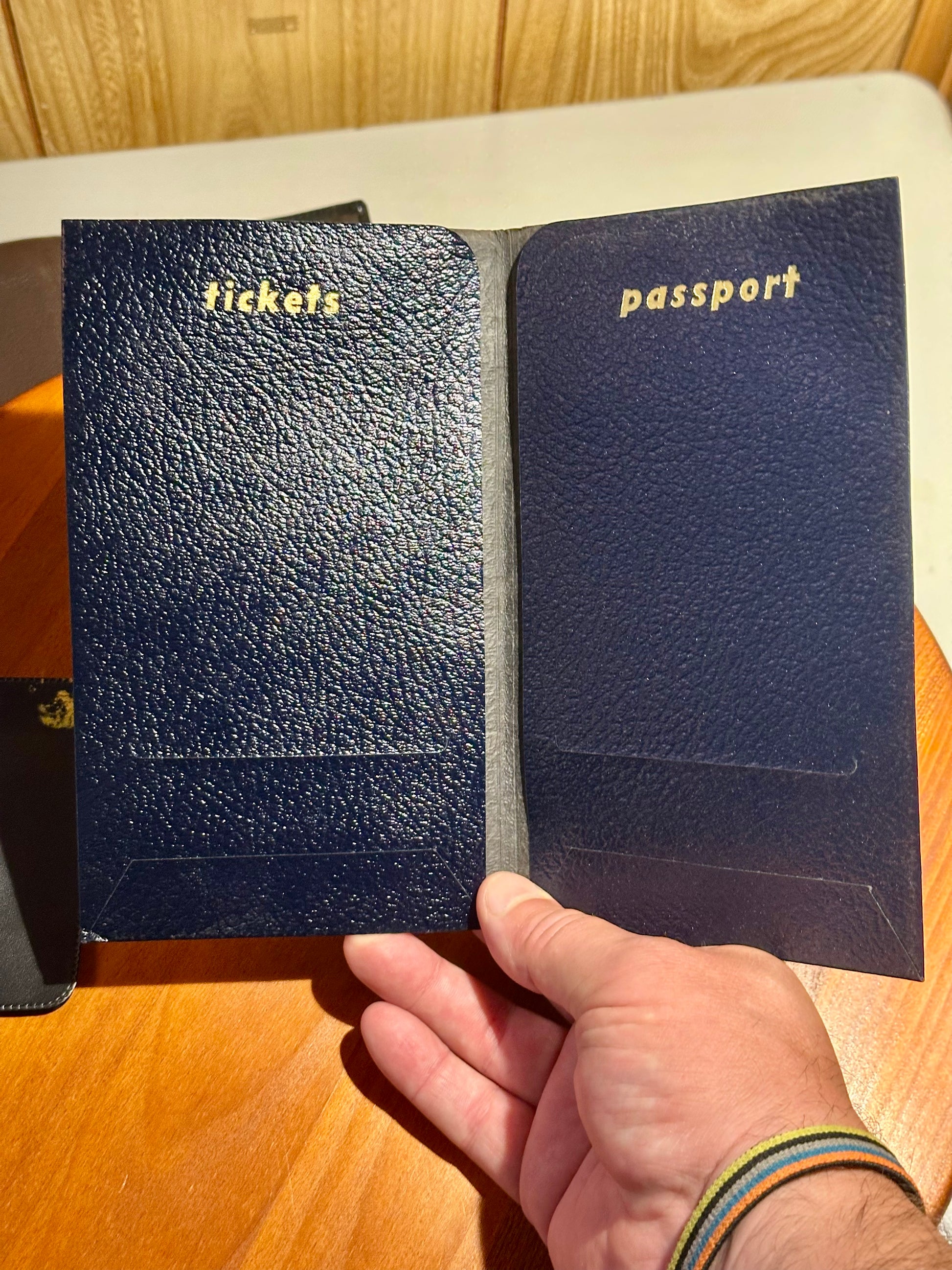 Two blue leather travel wallets labeled 'tickets' and 'passport' held by a hand on a wooden surface.