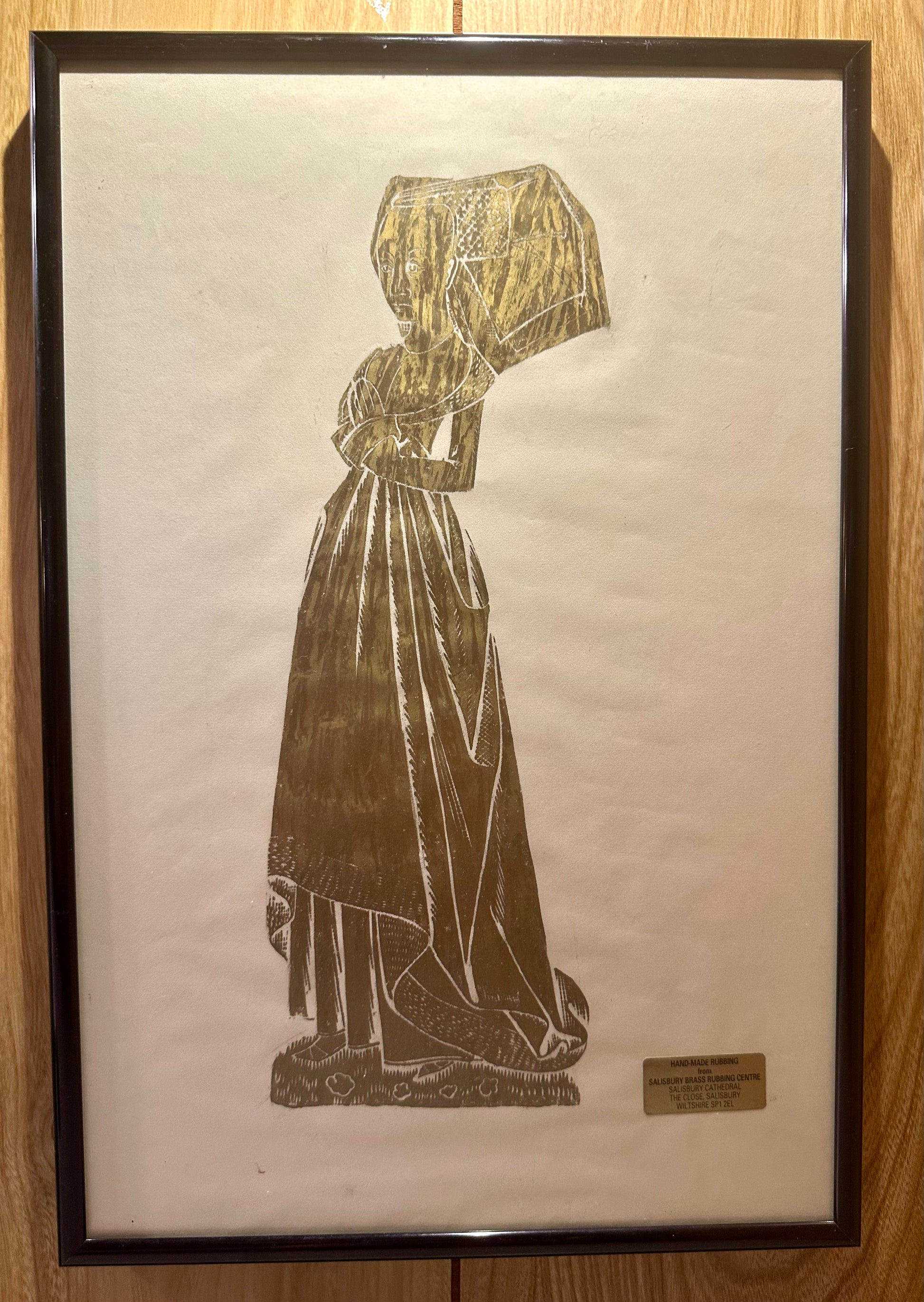 Framed artwork of a classical woman with a hood on a wooden surface