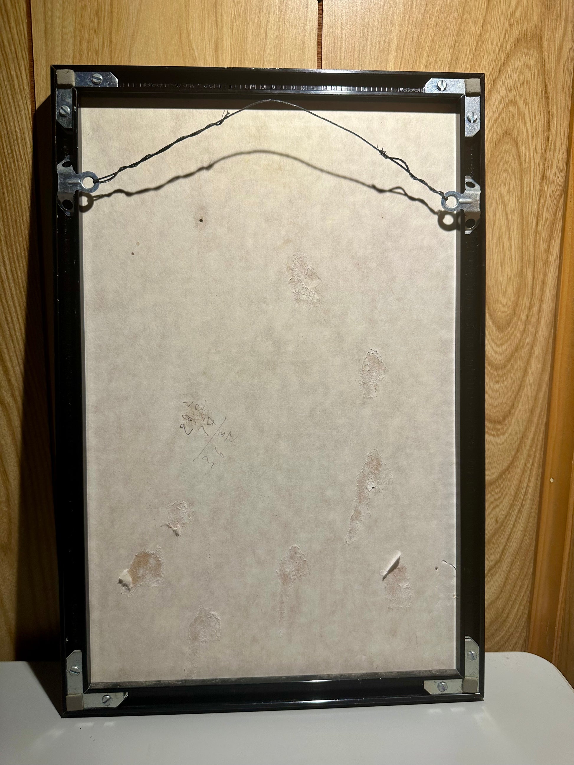 Backing of framed artwork with a textured beige center and black frame on a wooden surface.