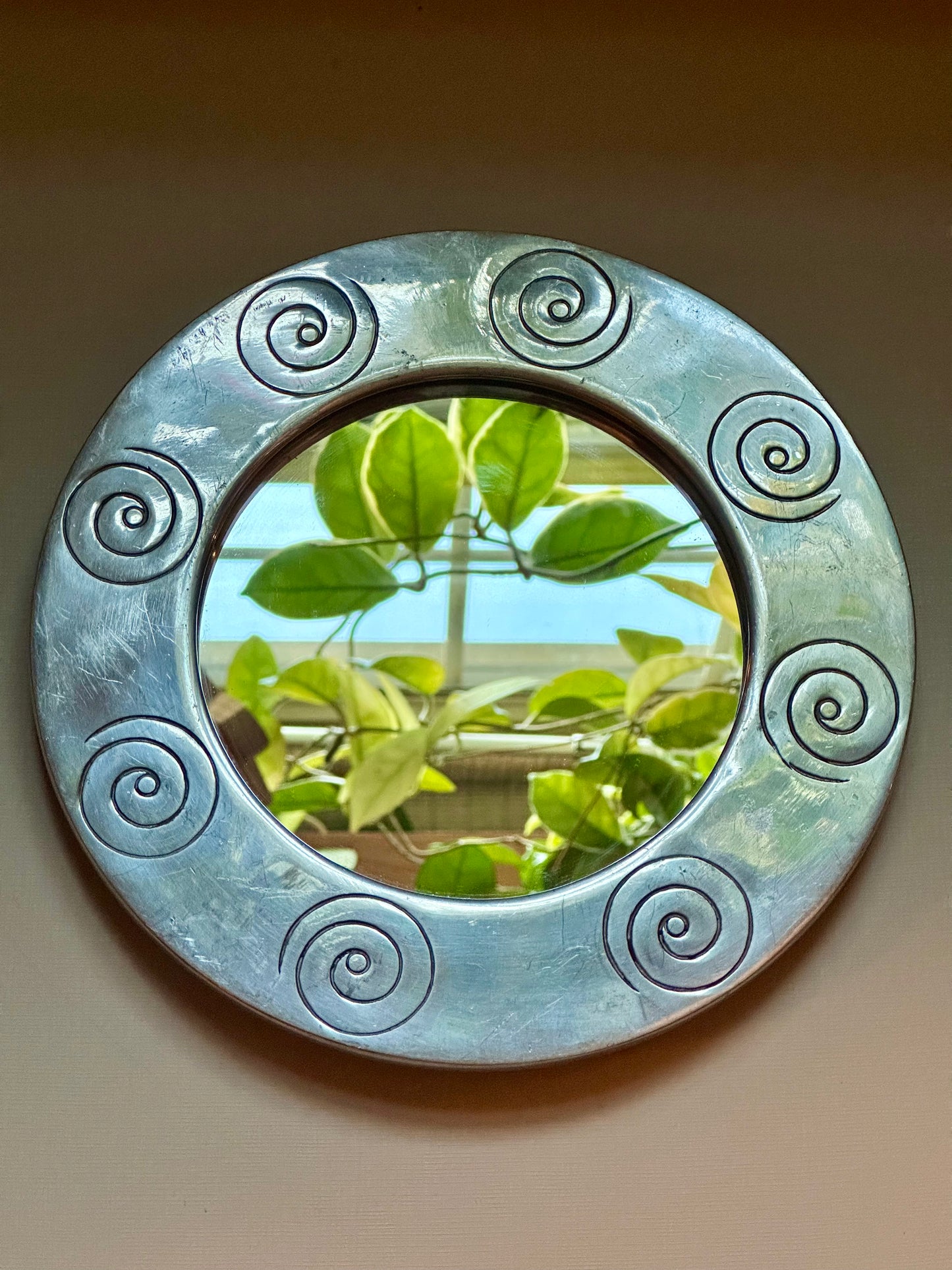 Round decorative mirror with spiral patterns reflecting green foliage