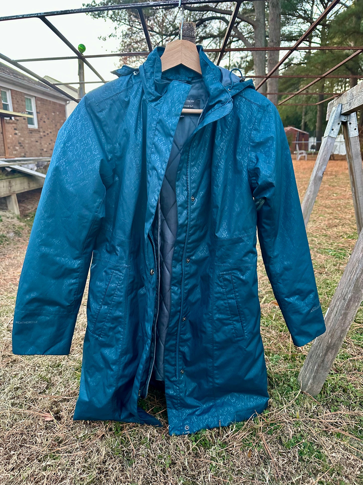 Blue raincoat hanging outdoors on a wooden hanger with a rustic background.