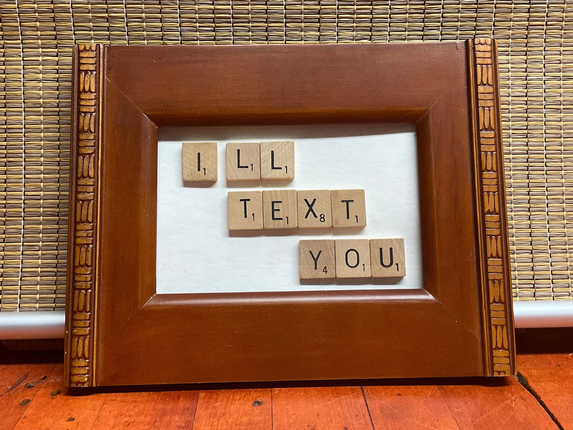 Brown wood frame with Scrabble tiles spelling out the phrase "I'll Text You" on a white background.