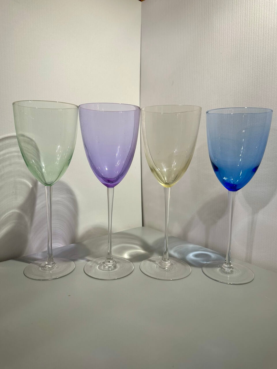 Four colorful wine glasses in a row on a white surface with a white background