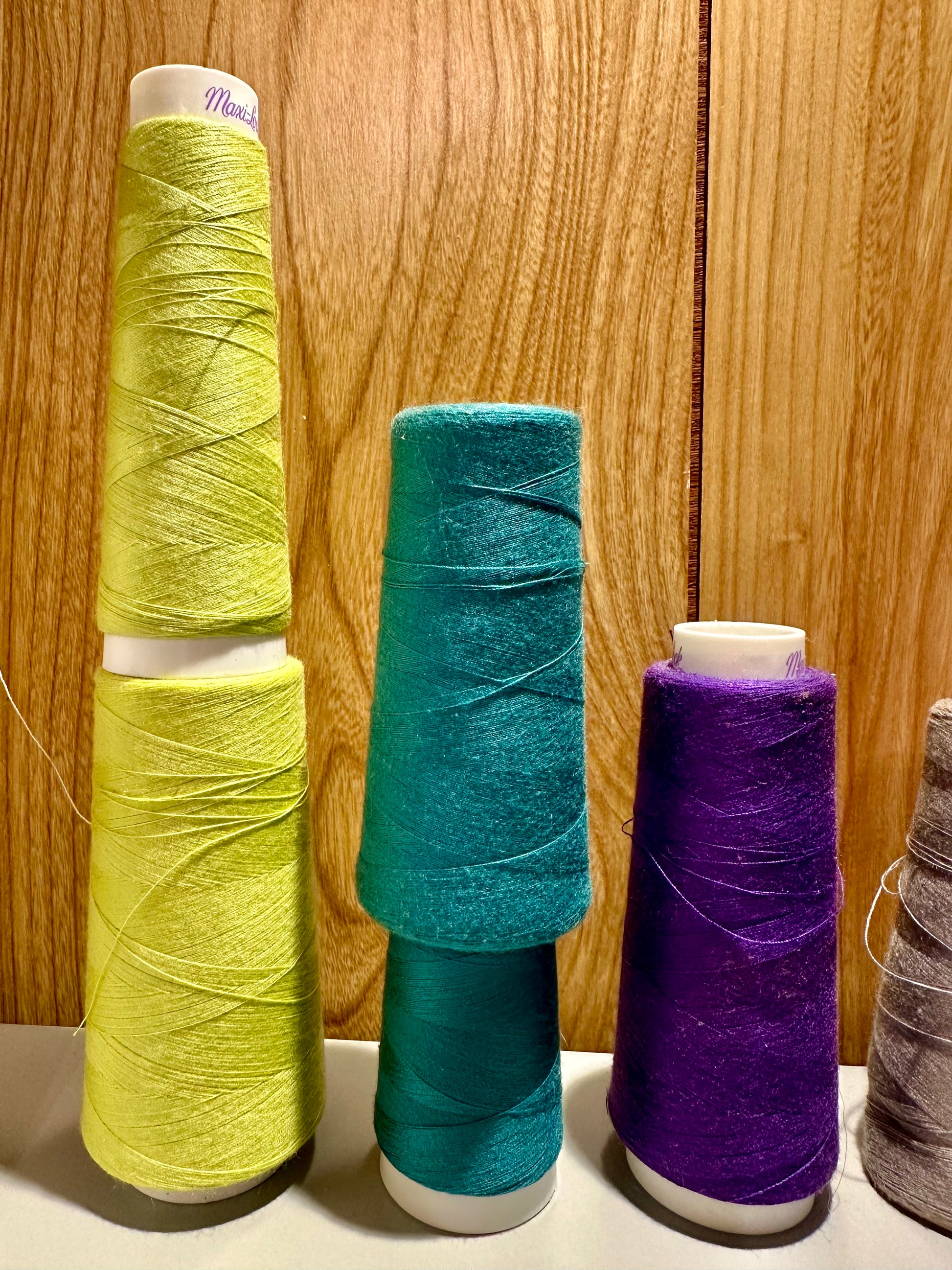 Three spools of thread in yellow, blue, and purple on a wooden surface.