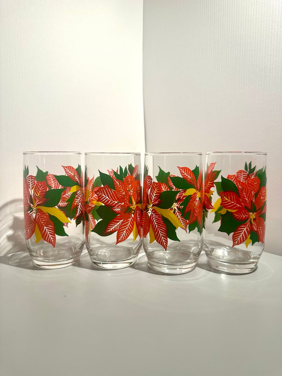 Four glass tumblers with poinsettia design on a white background