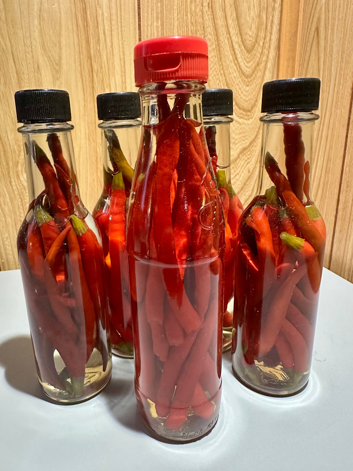 Bottles of red pepper vinegar with black lids on a wooden surface