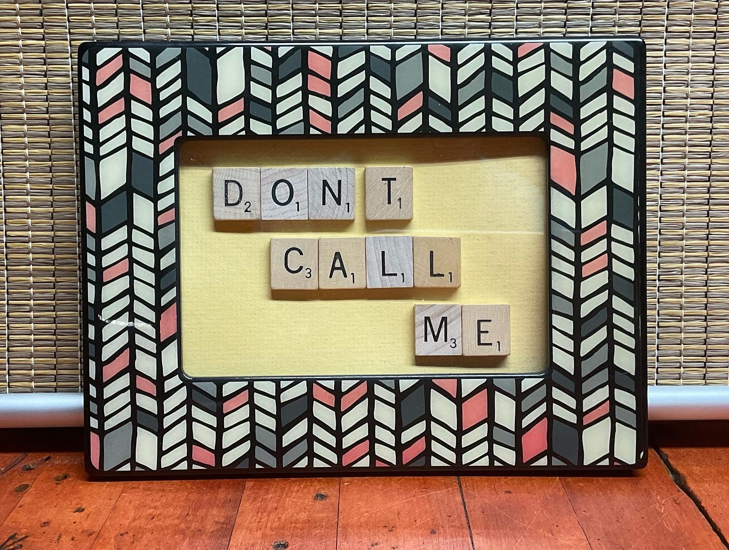 Decorative frame with scrabble tiles spelling 'DON'T CALL ME' on a wooden floor.