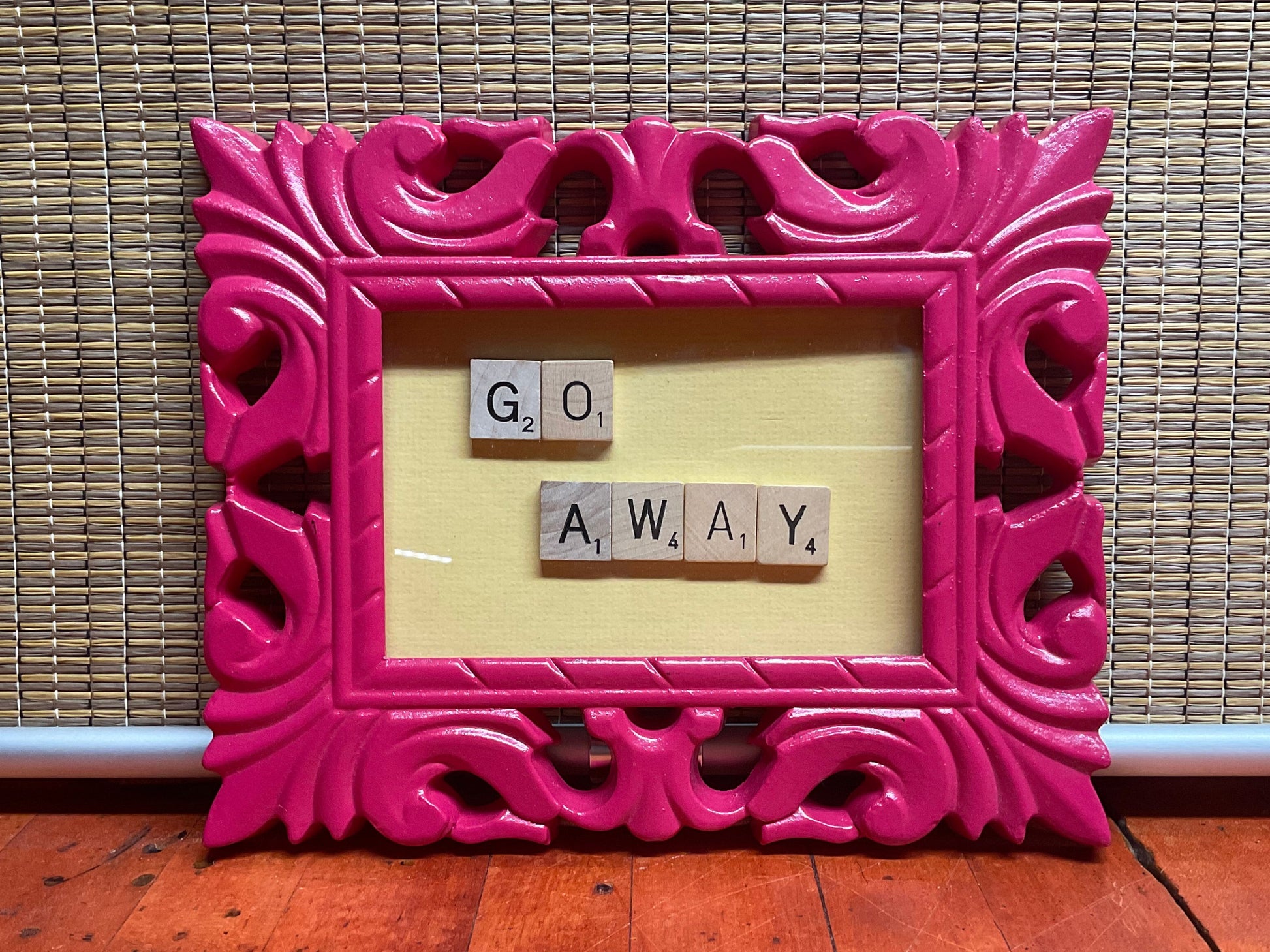 Pink frame with scrabble tiles on a yellow background spelling out the phrase 'Go Away'