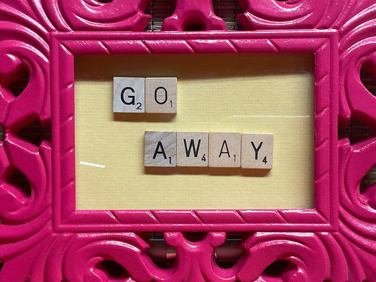 Pink decorative frame with 'GO AWAY' text on a wooden floor and woven wall background