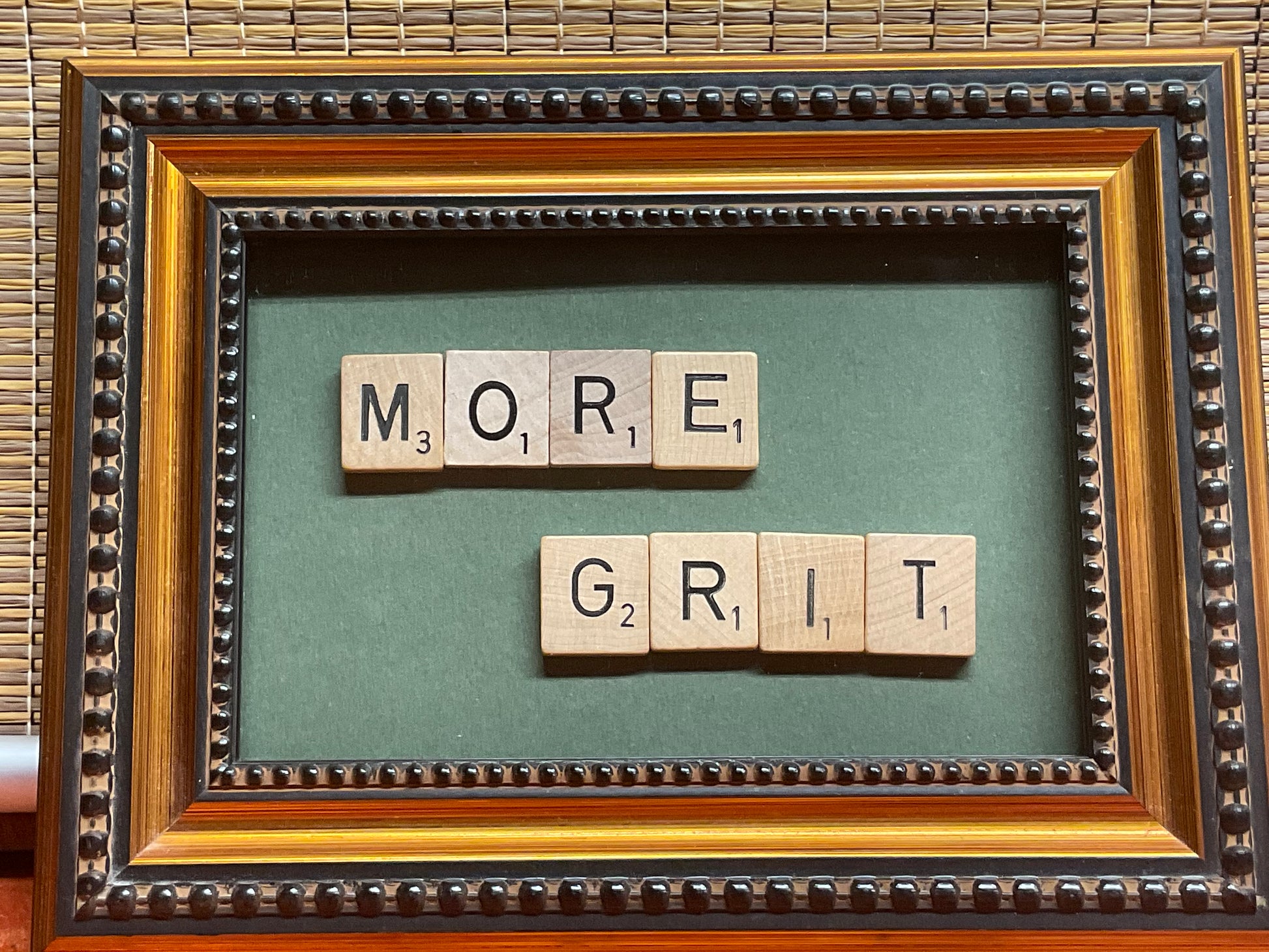 Framed artwork with scrabble tiles spelling 'MORE GRIT' on a green background.