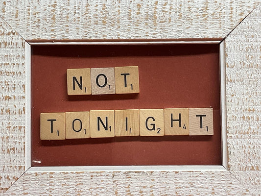 Wooden scrabble tiles spelling 'NOT TONiGHT' in a weathered frame.