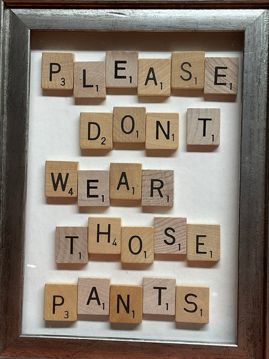 Framed artwork made of wooden scrabble tiles with a message.