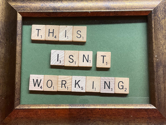 Wooden scrabble tiles spelling 'THIS ISN'T WORKING' in a wooden frame.