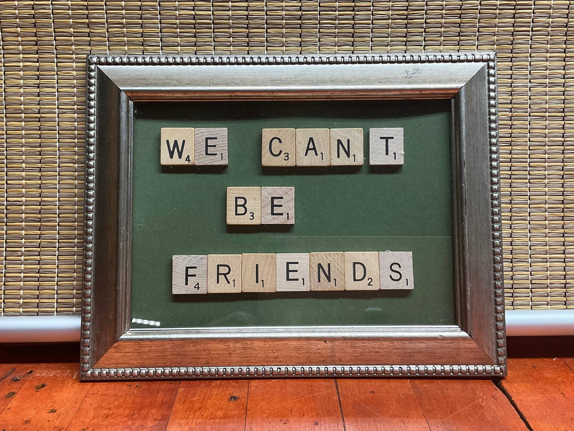 Silver beaded frame with scrabble tiles on green mat board spelling out "we can't be friends"