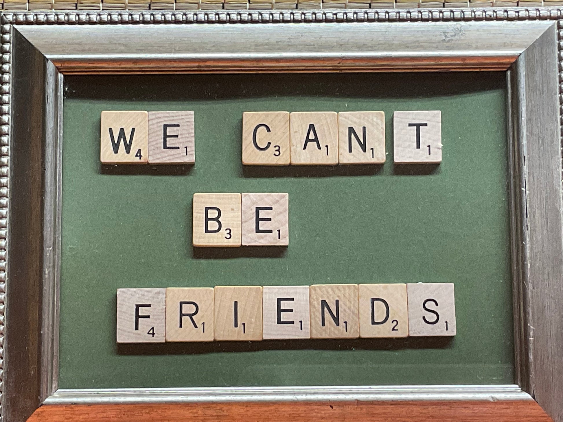 Framed artwork with Scrabble tiles spelling 'WE CAN'T BE FRIENDS' on a green background