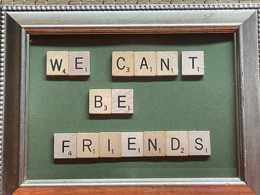 Framed artwork with Scrabble tiles spelling 'WE CAN'T BE FRIENDS' on a green background