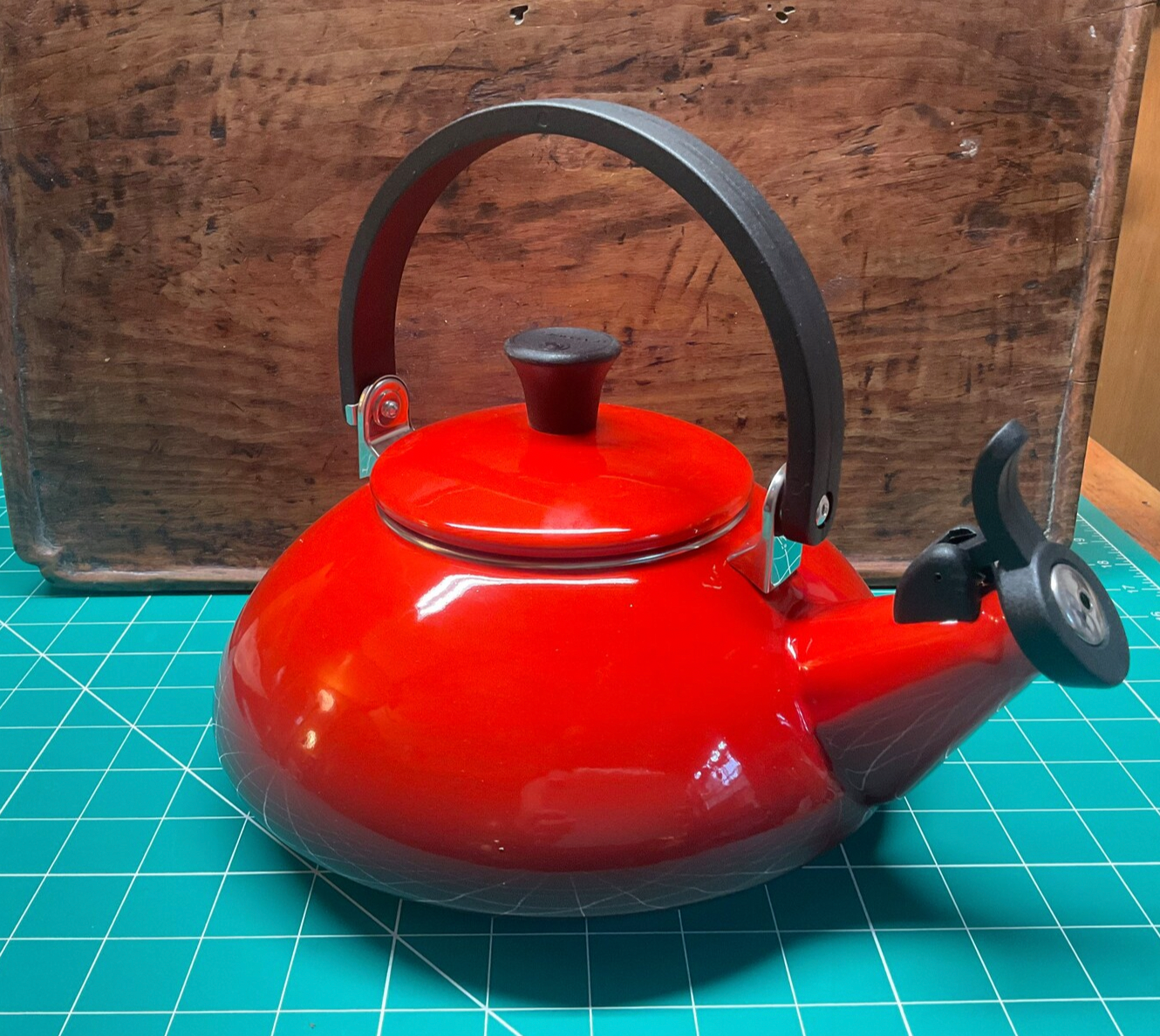 Red kettle with black handle and lid knob on a blue grid surface