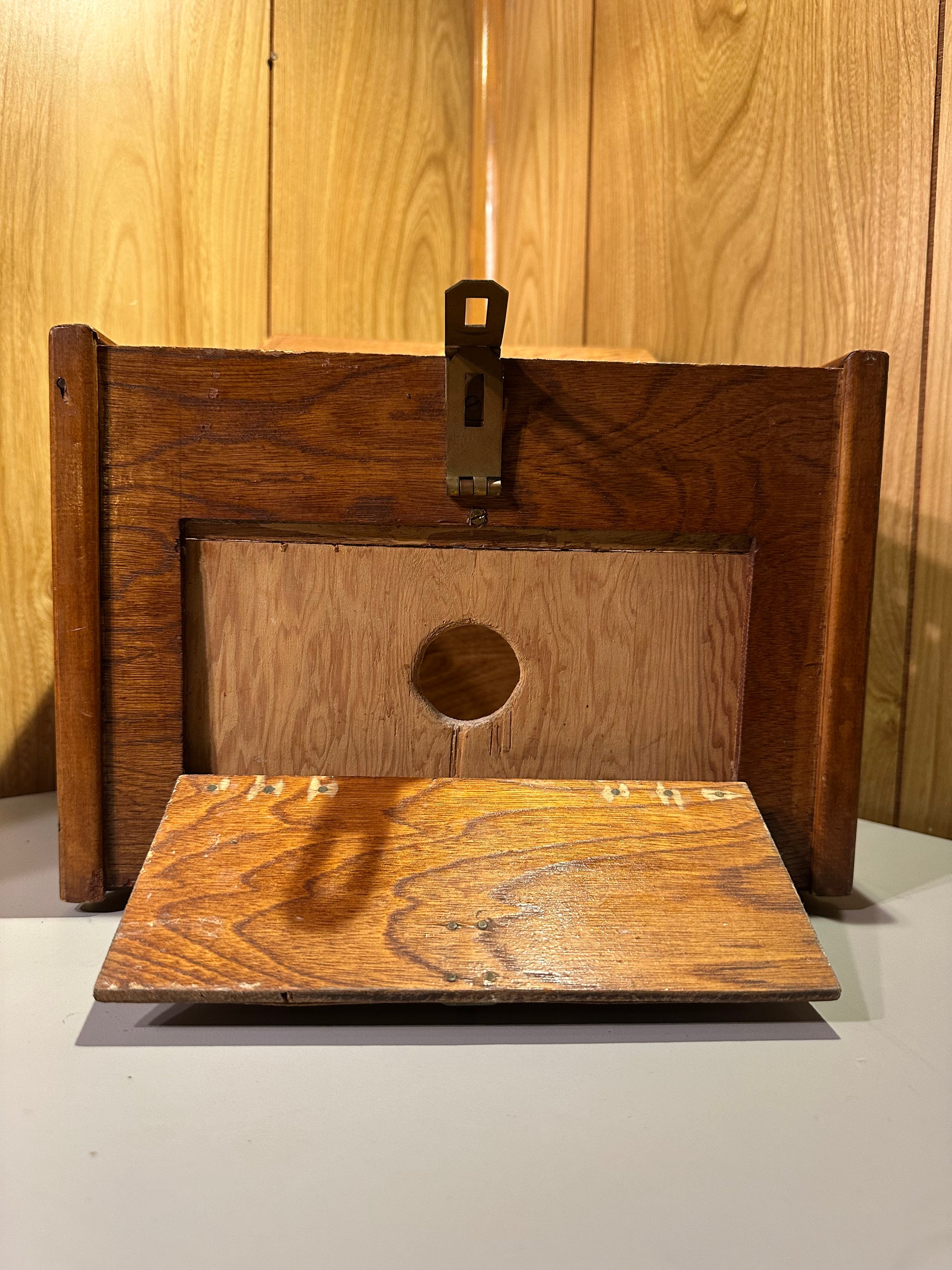 Wooden specimen box on a wood background with front flap folded down and showing a 1.5" hole.