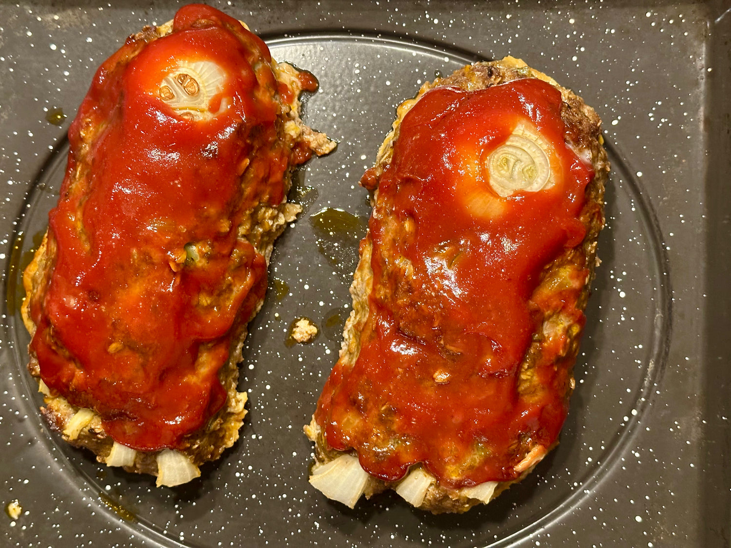 Two meatloaves with tomato sauce on a baking tray