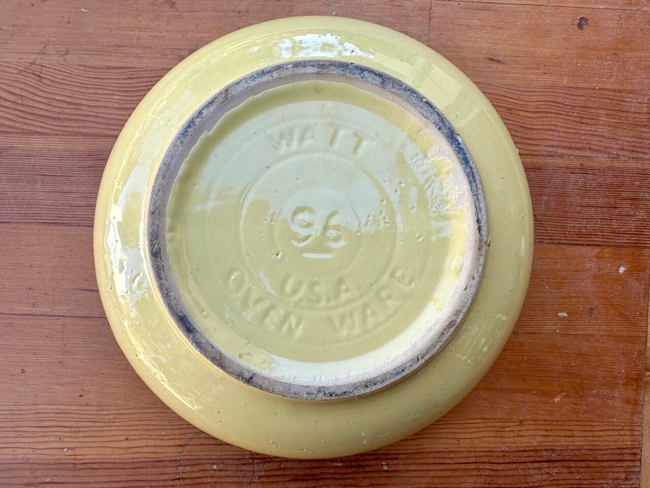 Yellow ceramic plate with a visible brand logo on a wooden surface