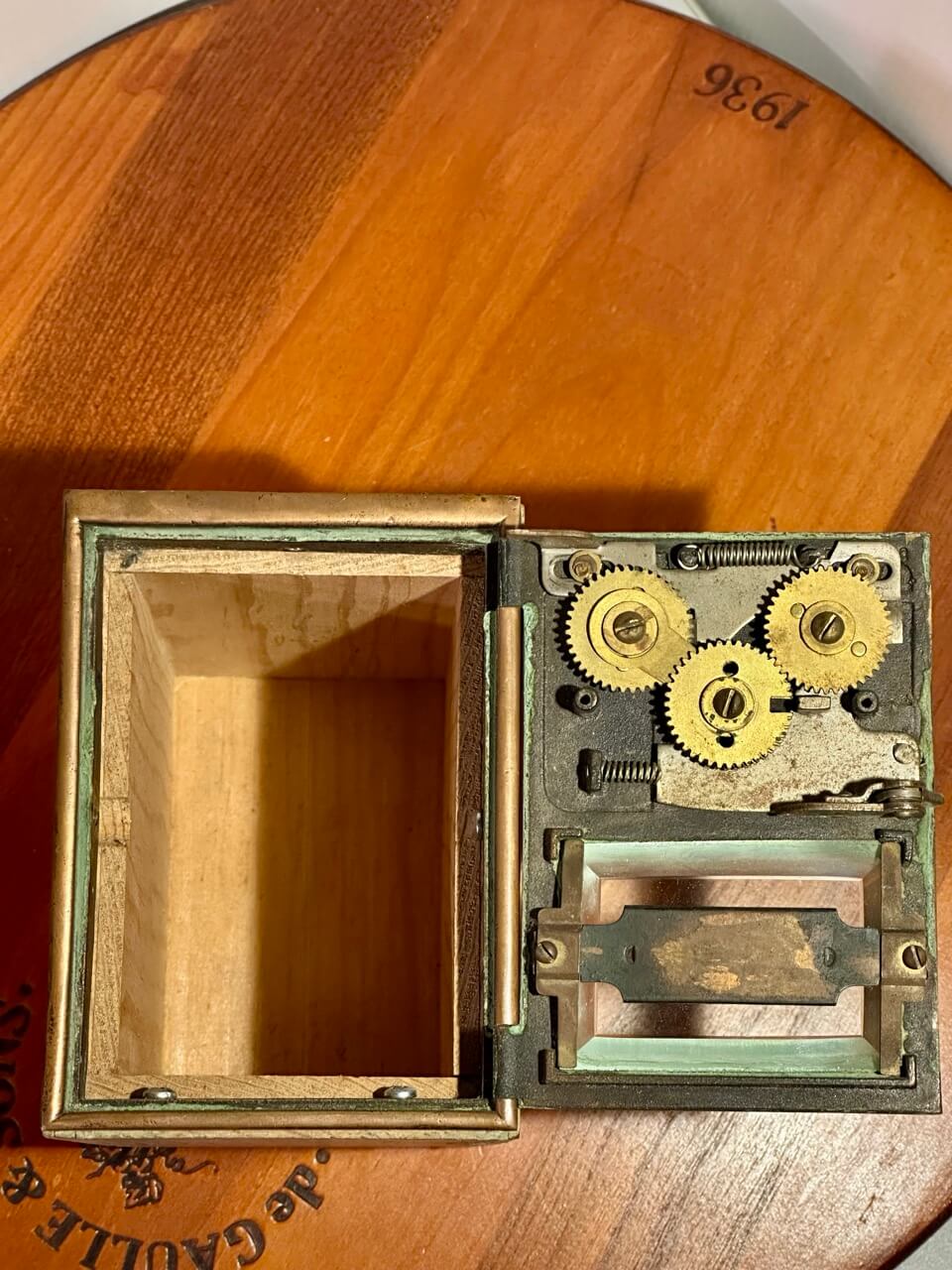 Wooden box with open lid revealing mechanical gears inside, on a wooden surface.