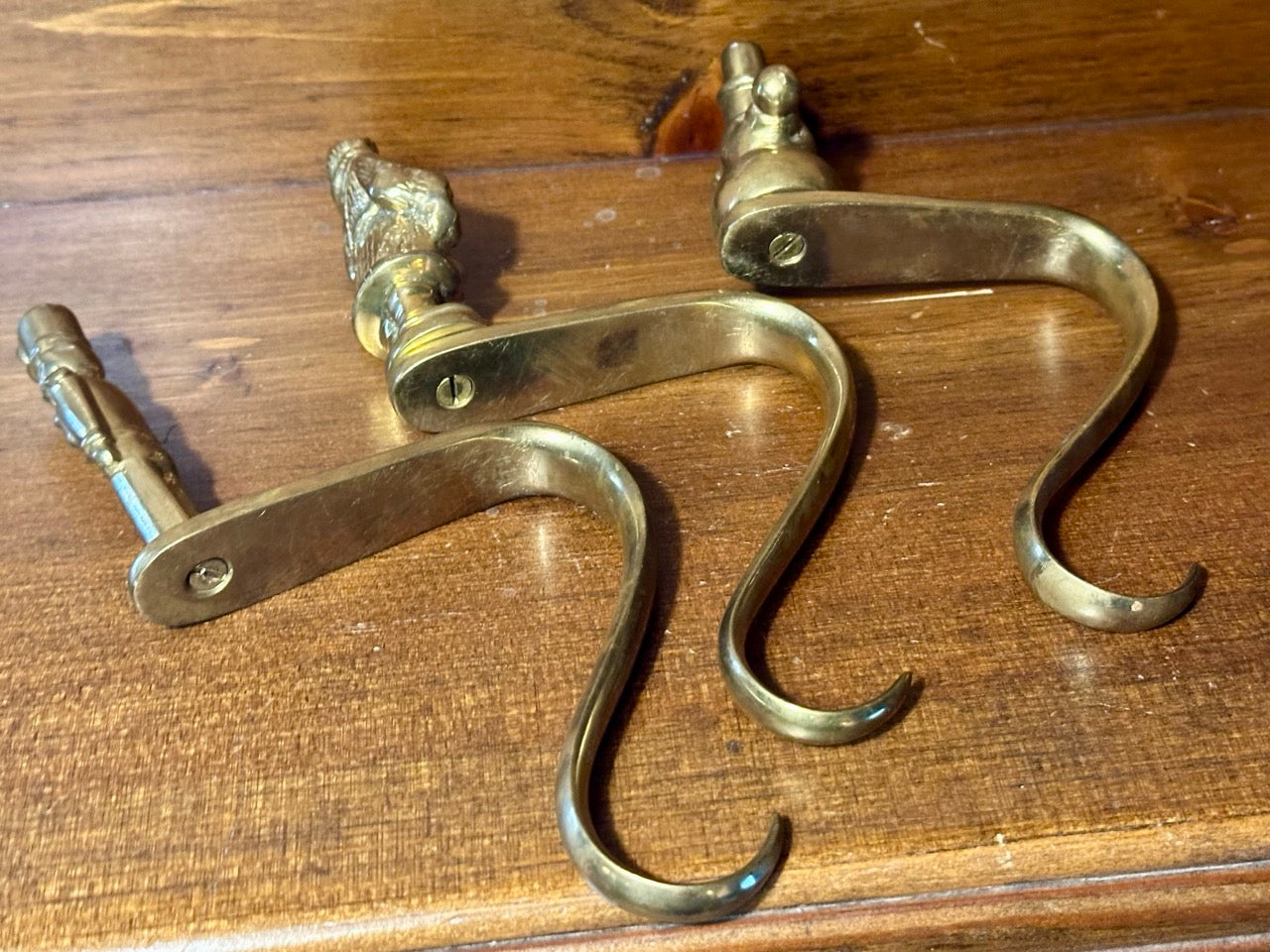 Three brass stocking hooks laying on their sides on a wooden surface.