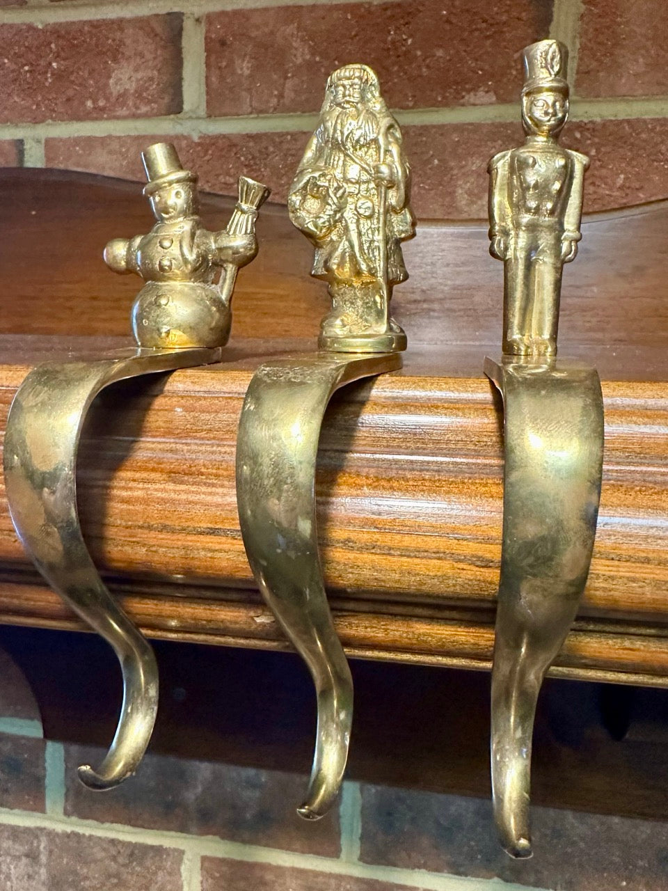Three decorative brass stocking hooks in a line with brick background. 