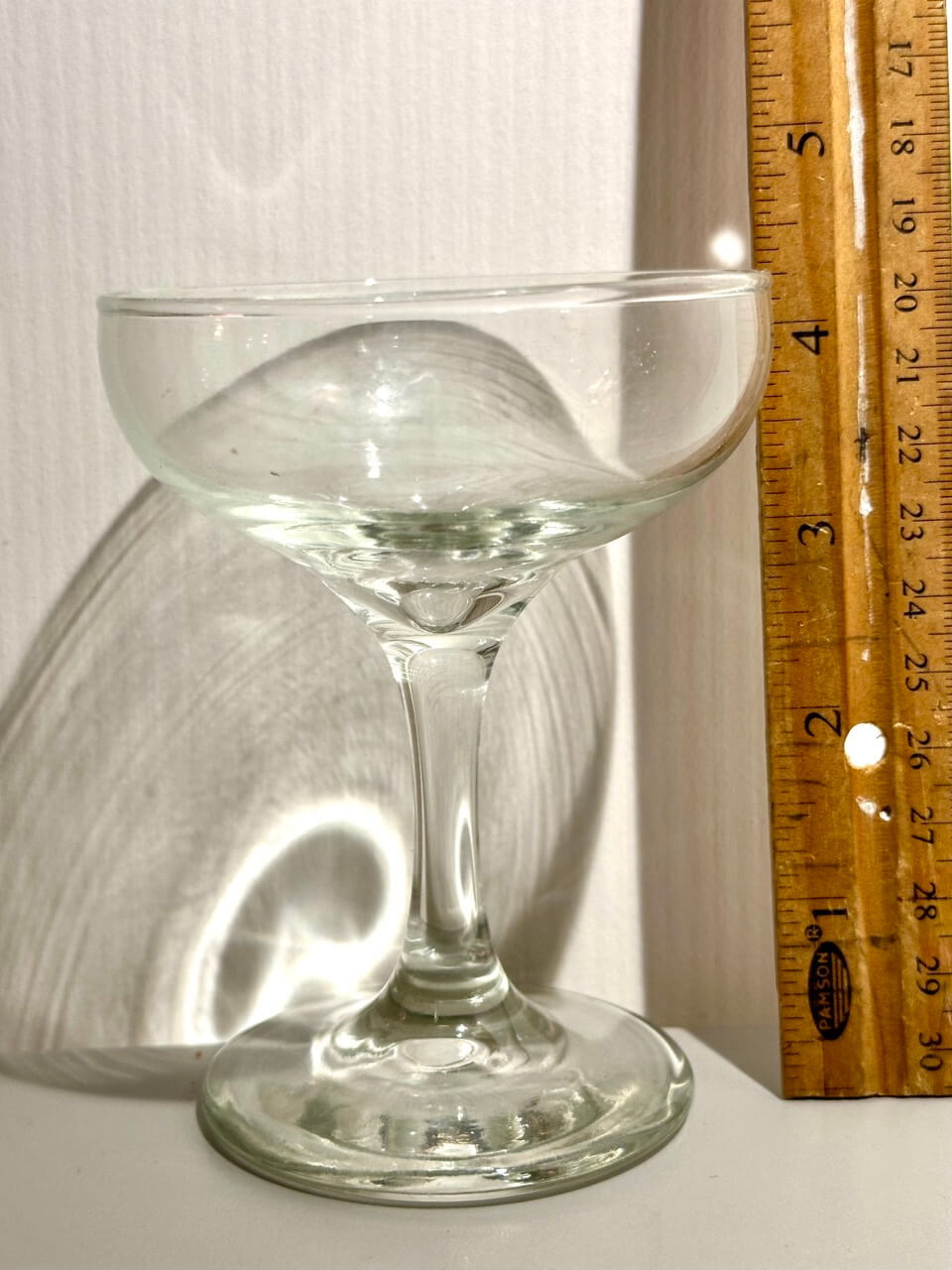 Clear glass cocktail glass next to a wooden ruler for scale