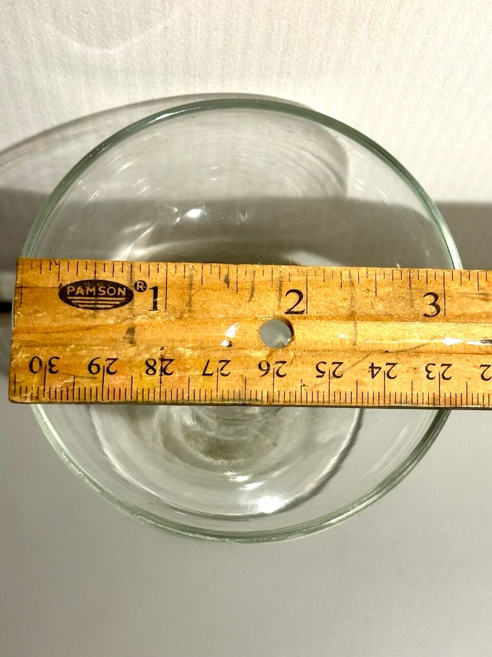 Clear cocktail glass with a wooden ruler for scale on a white background