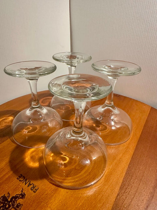 Four coupe champagne glasses upside down on a wooden surface.